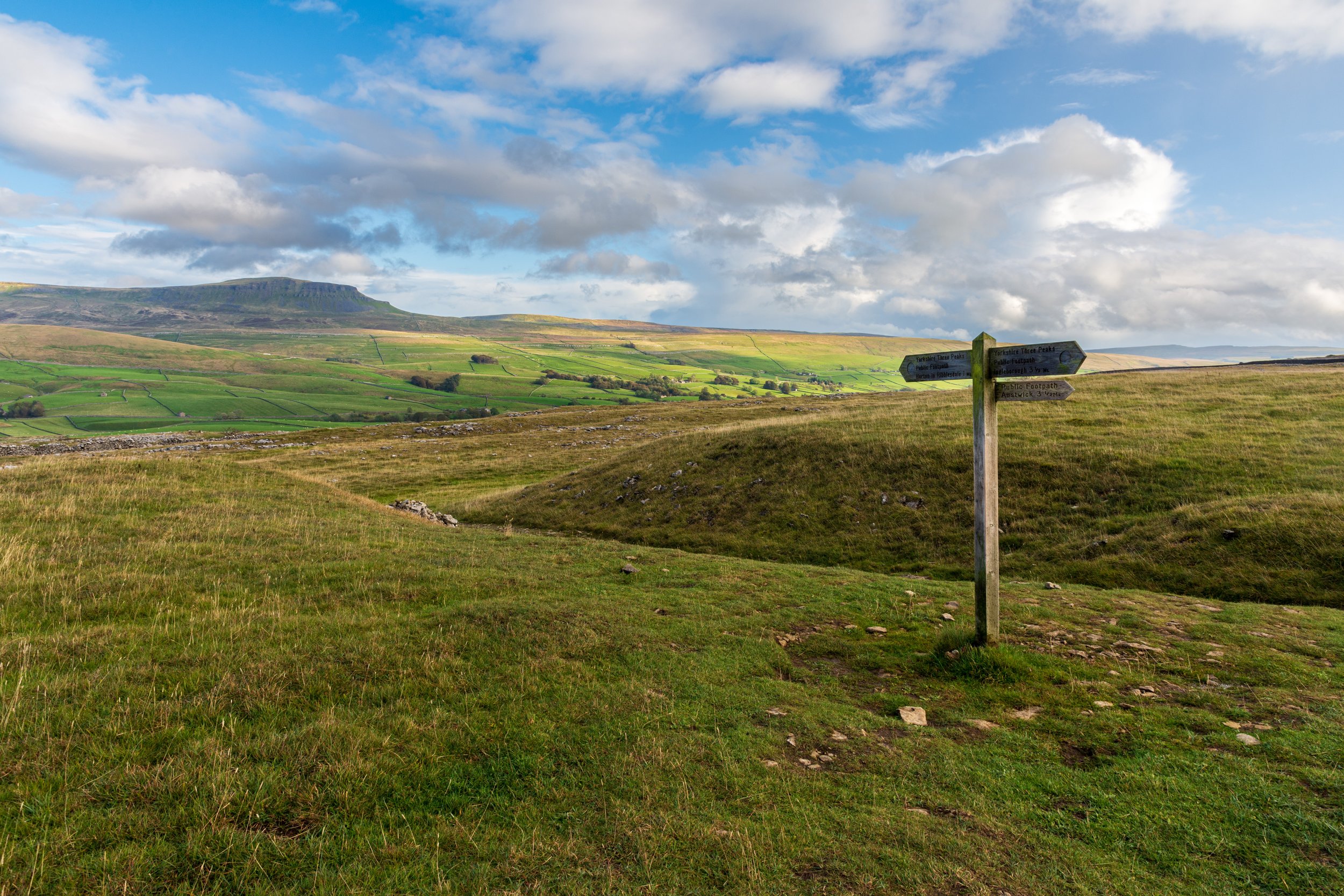 A sign post on the Yorkshire Three Peaks path, pointing towards Horton-in-Ribblesdale, with Pen-y-Ghent in the background