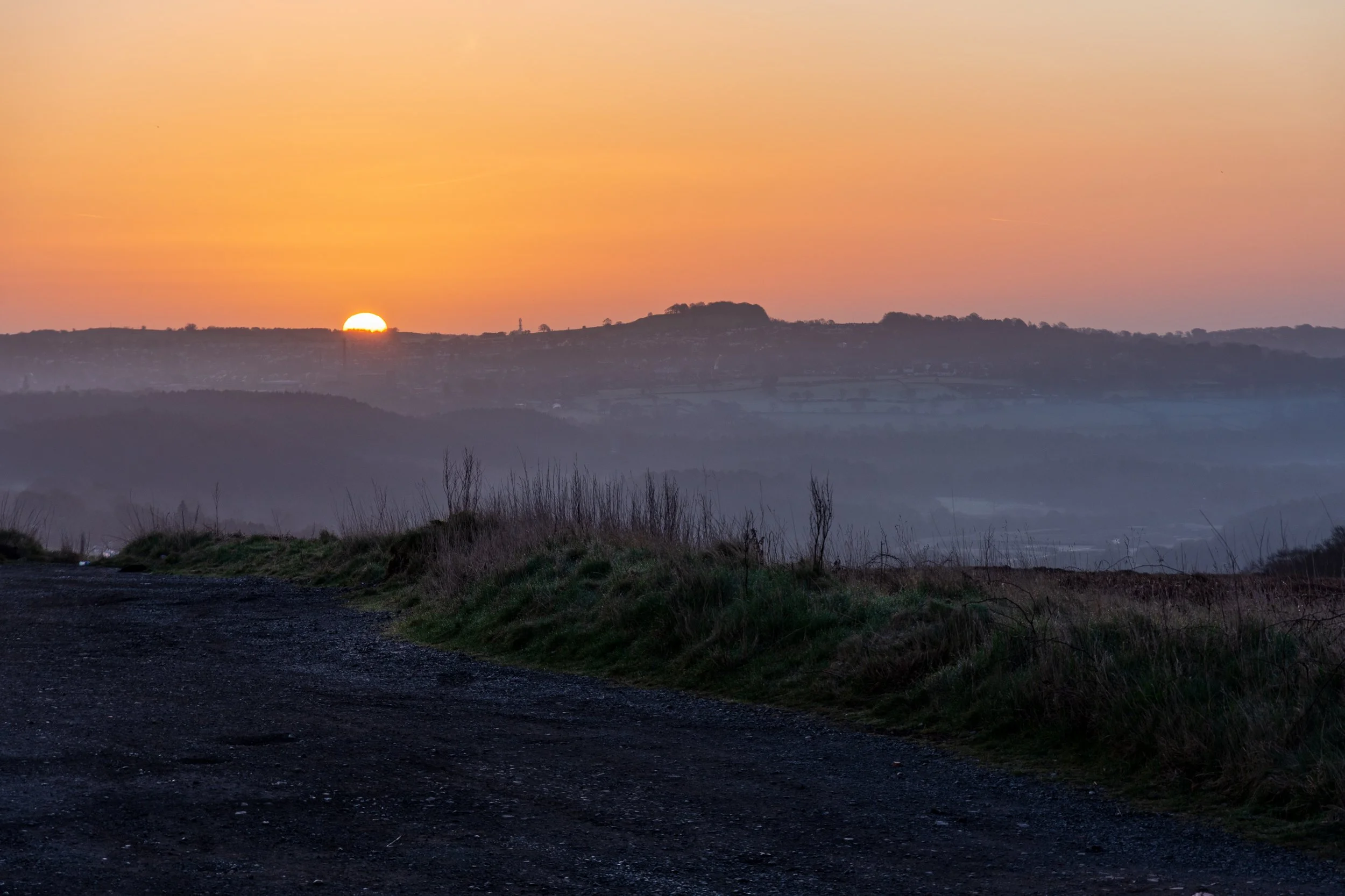 The sun rising in an orange sky over The Billing, Leeds, viewed from Baildon Hill