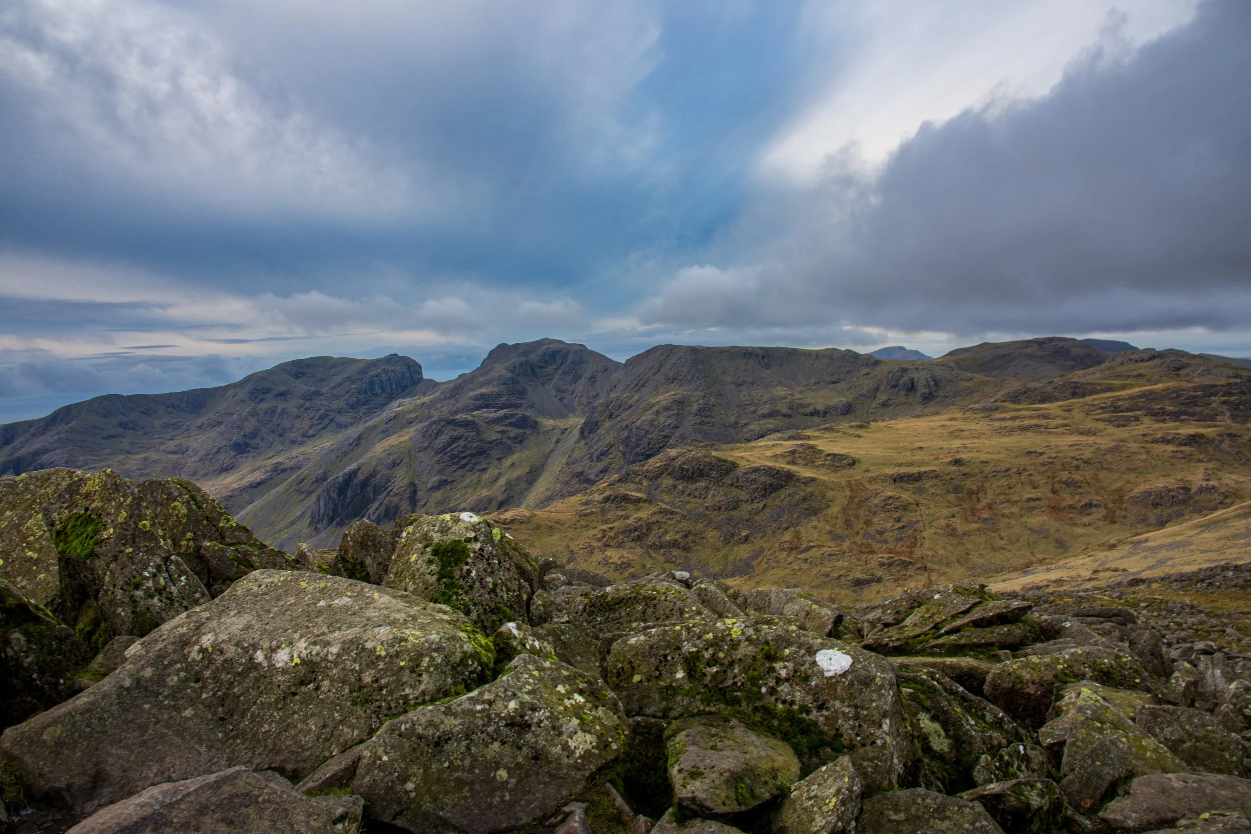 A view of Scafell and Scafell Pike in the Lake District, from the rocky summit of Bowfell, under broken clouds