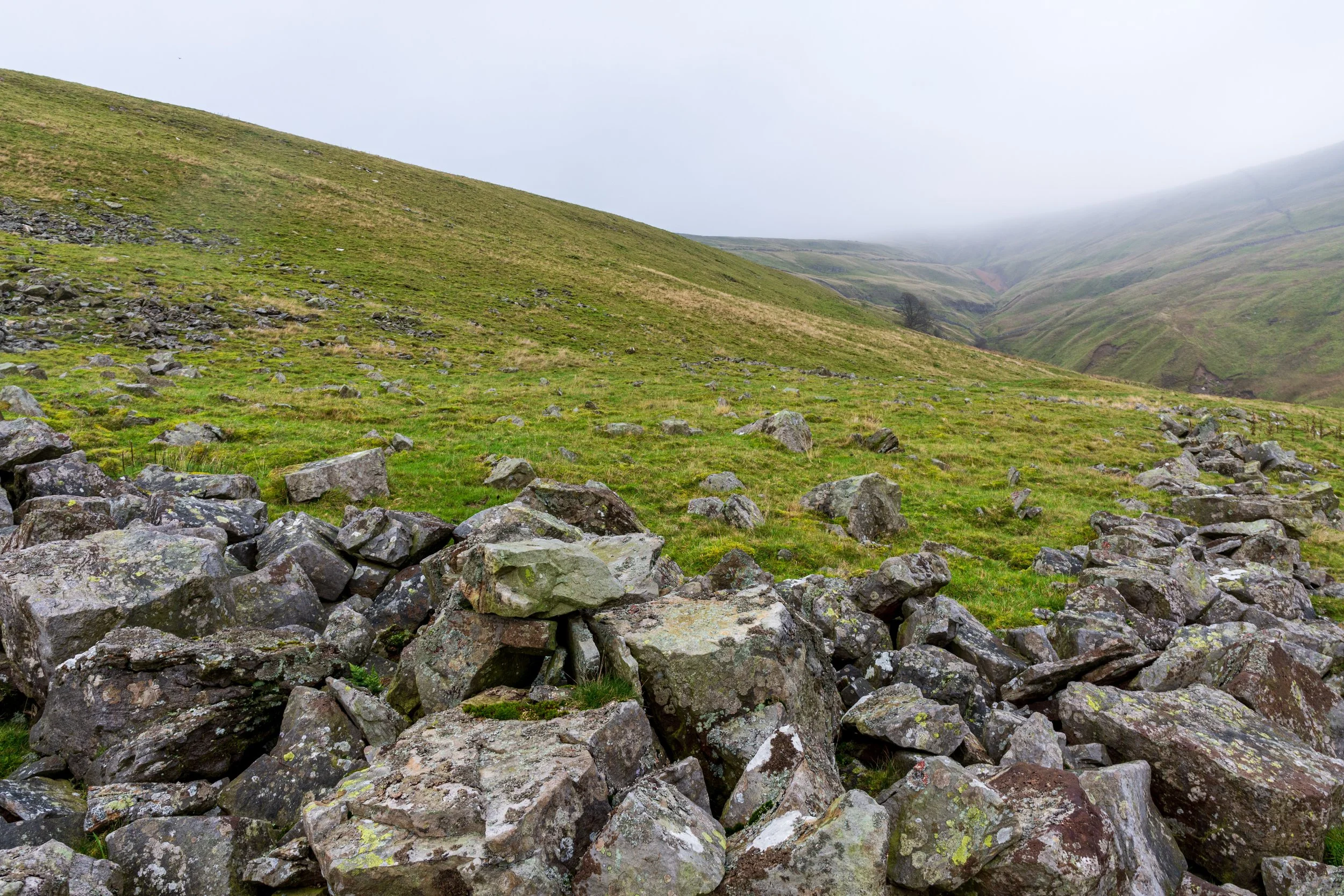 The rocky remains of a settlement on the approach to Buckden Pike summit, lining Buckden Beck, with the summit shrouded in mist.