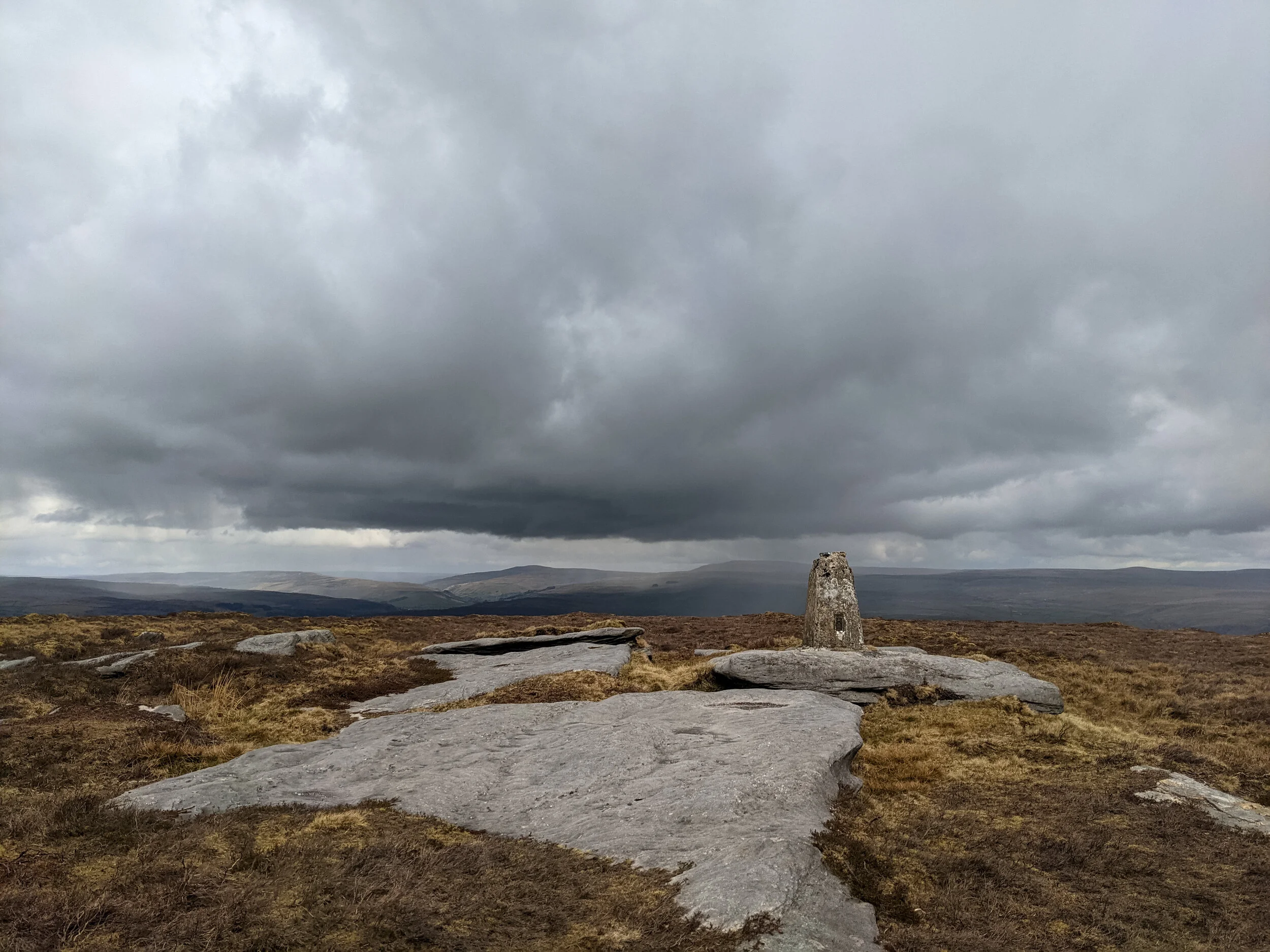 The lonely and forgotten trig point at Thorpe Fell Top, on Barden Moor, near Cracoe Fell, looking out to the Yorkshire Dales and Nidderdale, against a stormy sky