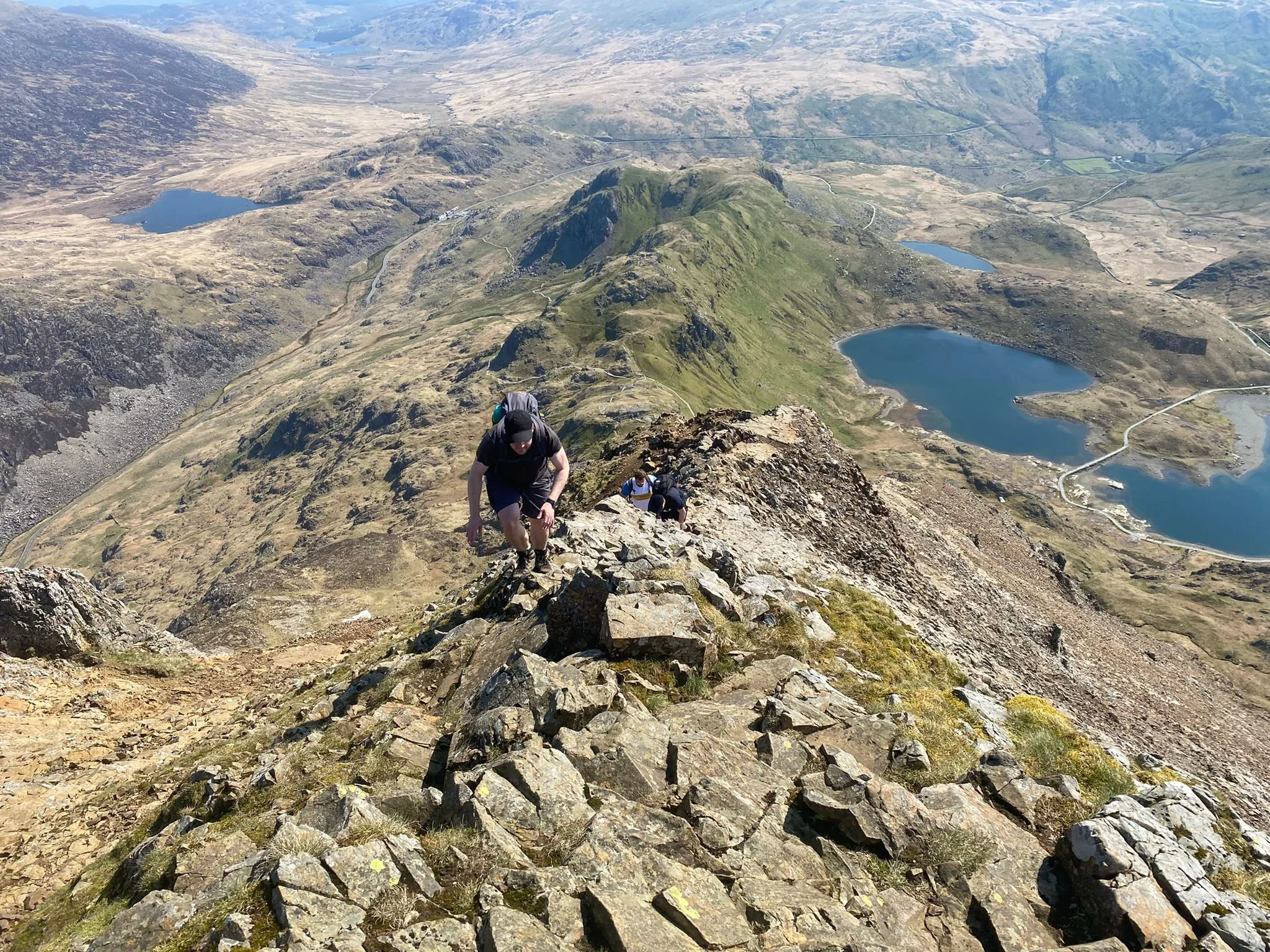 Ant climbing up to the Crib Goch summit on exposed path, with Llyn Llydaw, Llyn Teryn, Llyn Cwmffynnon and Pen-y-pass in the background