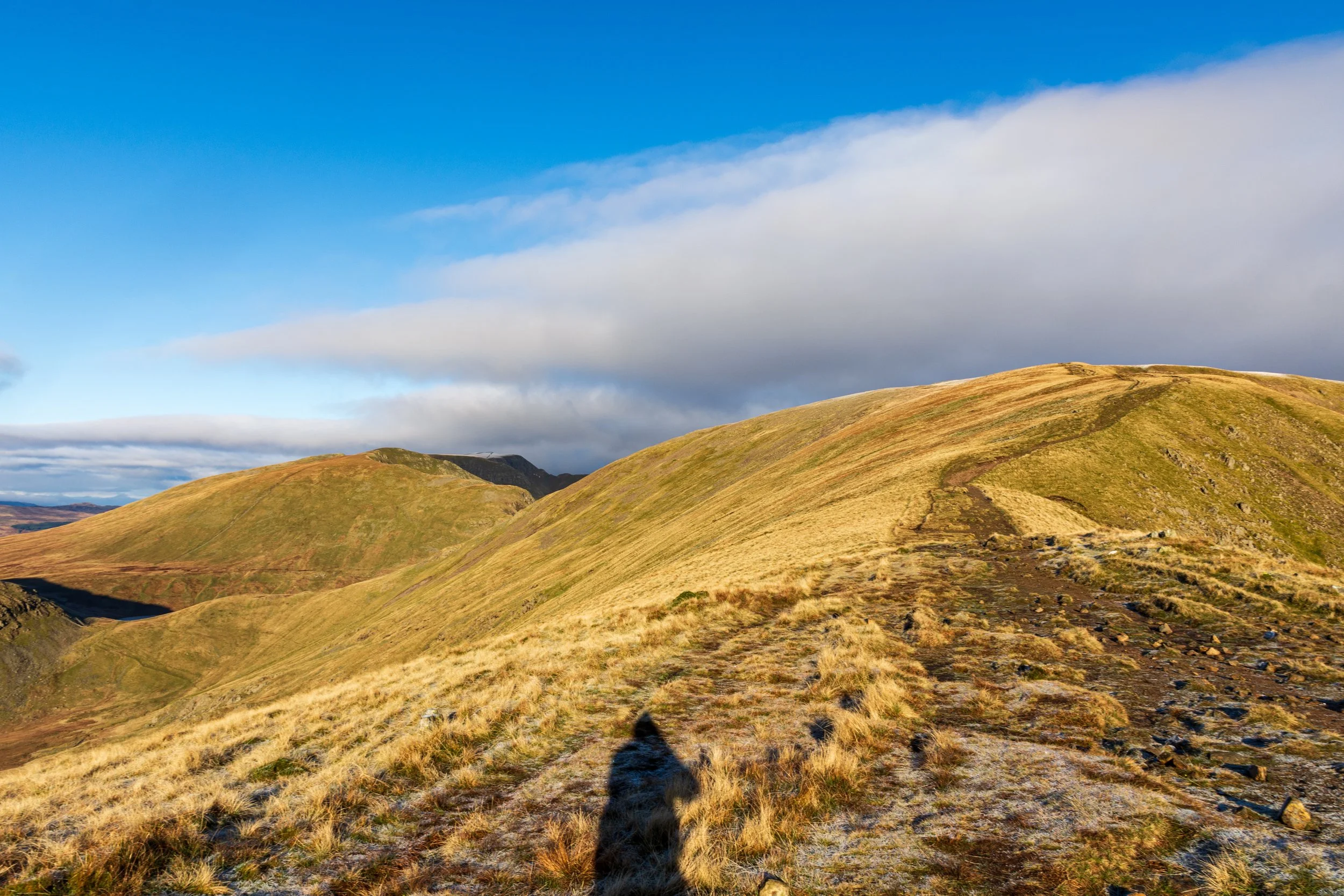 Path towards the summit of Fairfield in the Lake District, from Great Rigg, on sunny day with cloud moving in, photographer's shadow in the foreground