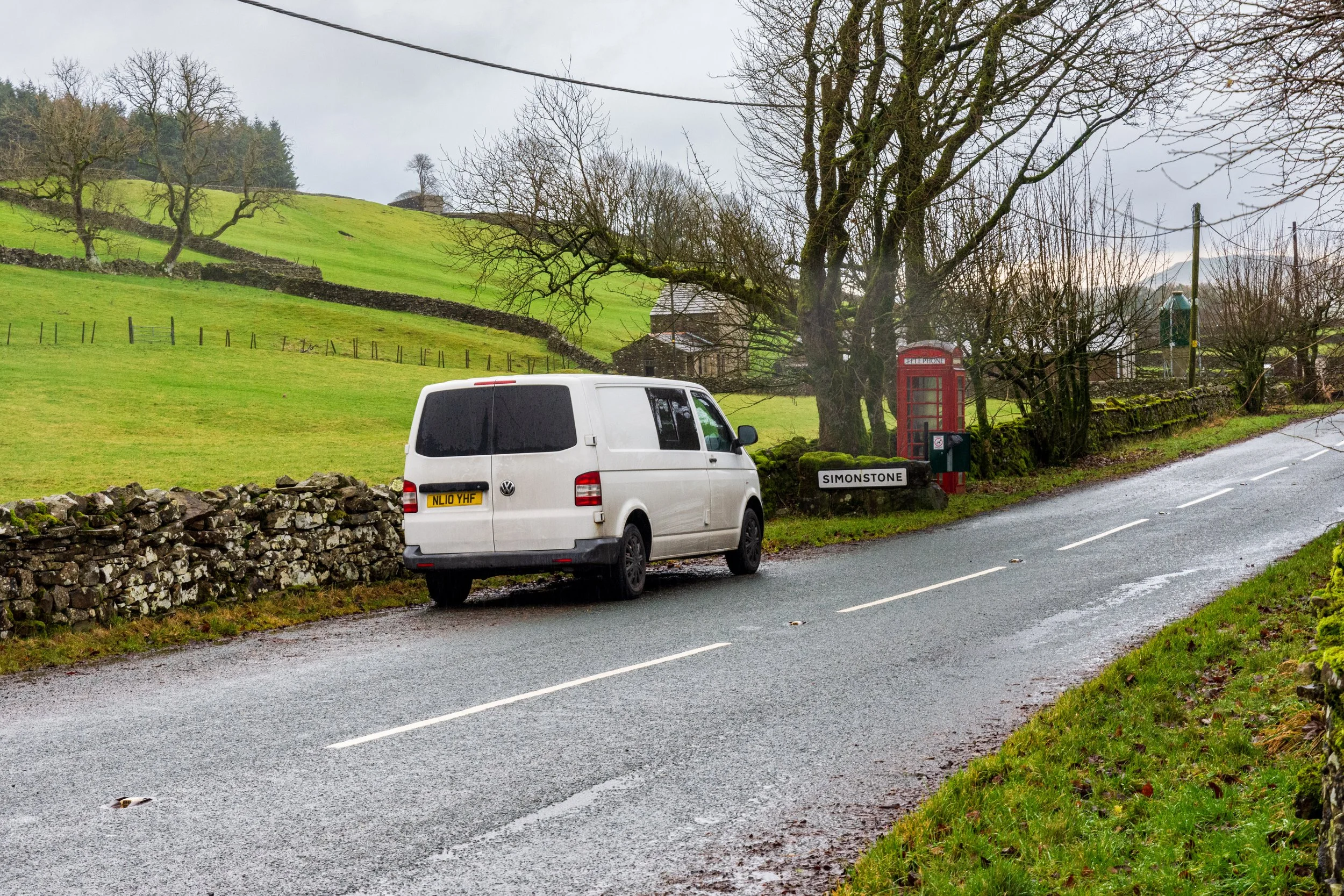 White VW Transporter T5.1 campervan parked in a layby in Simonstone in the Yorkshire Dales, at the foot of Lovely Seat, next to a red British telephone box