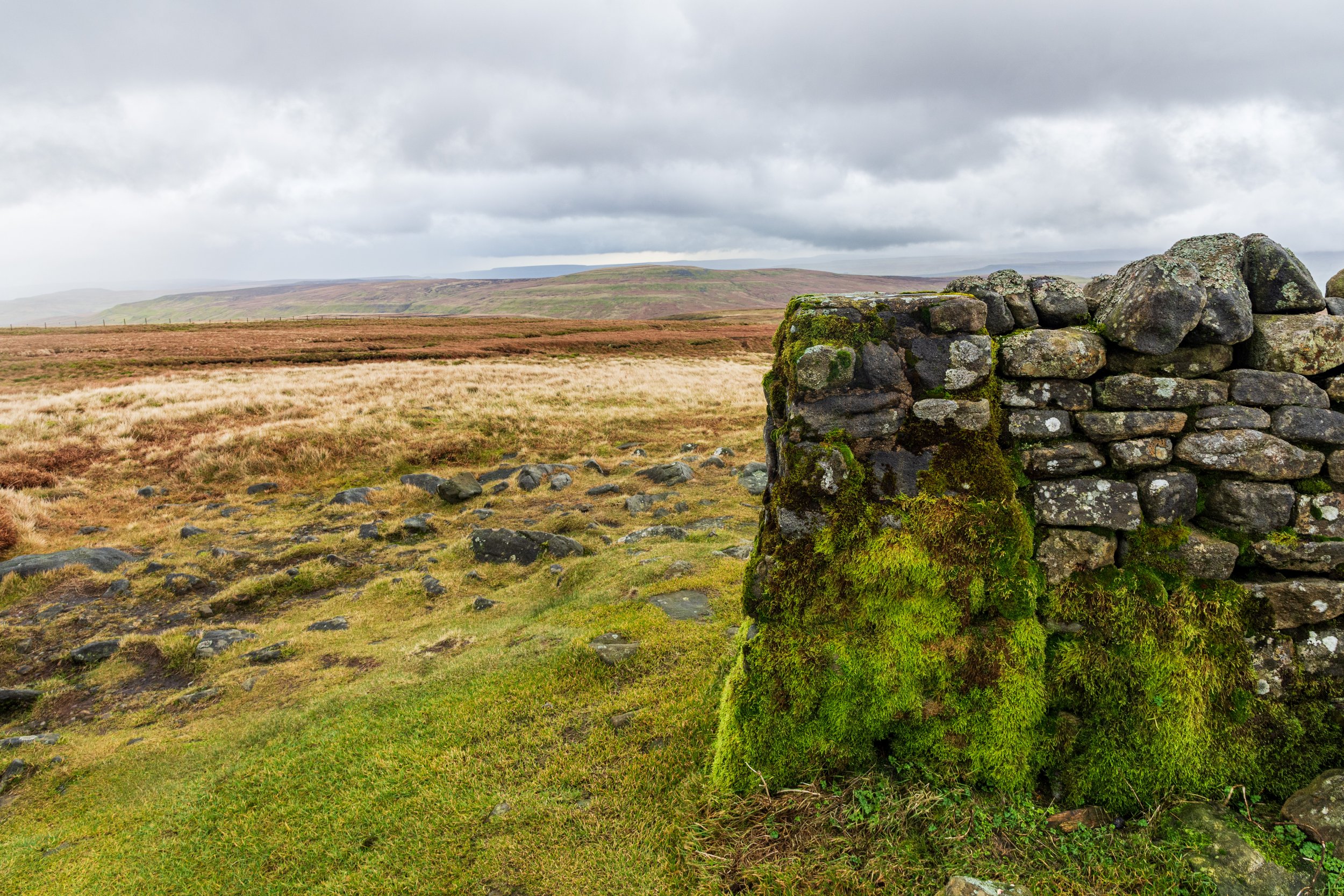 A trip pillar built into a summit shelter on the summit of Great Shunner Fell, looking across open moorland to the Butter Tubs pass and Lovely Seat in the Yorkshire Dales