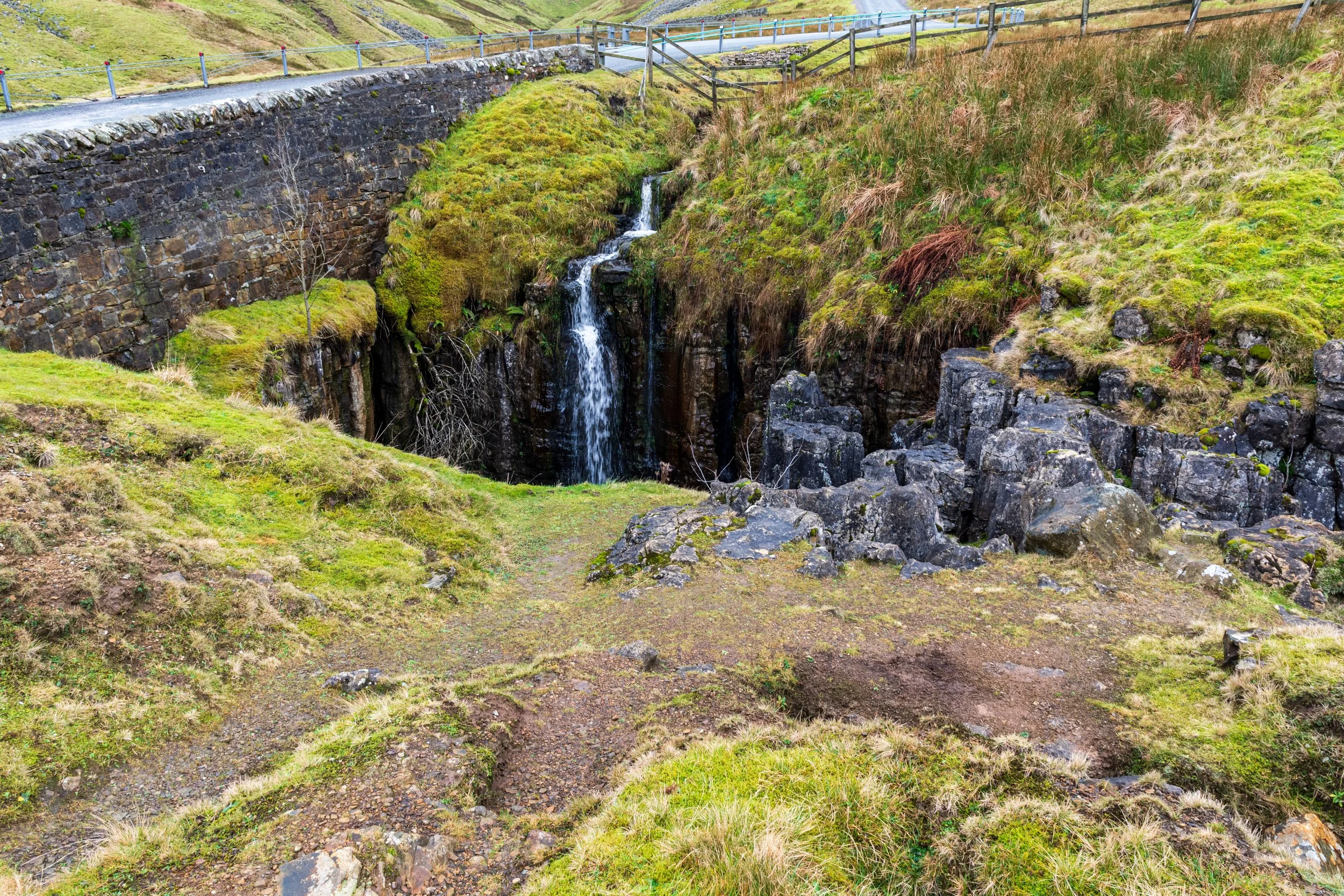 View of the Butter Tubs hole, with the Buttertubs pass between Muker and Hawes in the background, lying between Great Shunner Fell and Lovely Seat. Water is flowing into the hole on a wet day