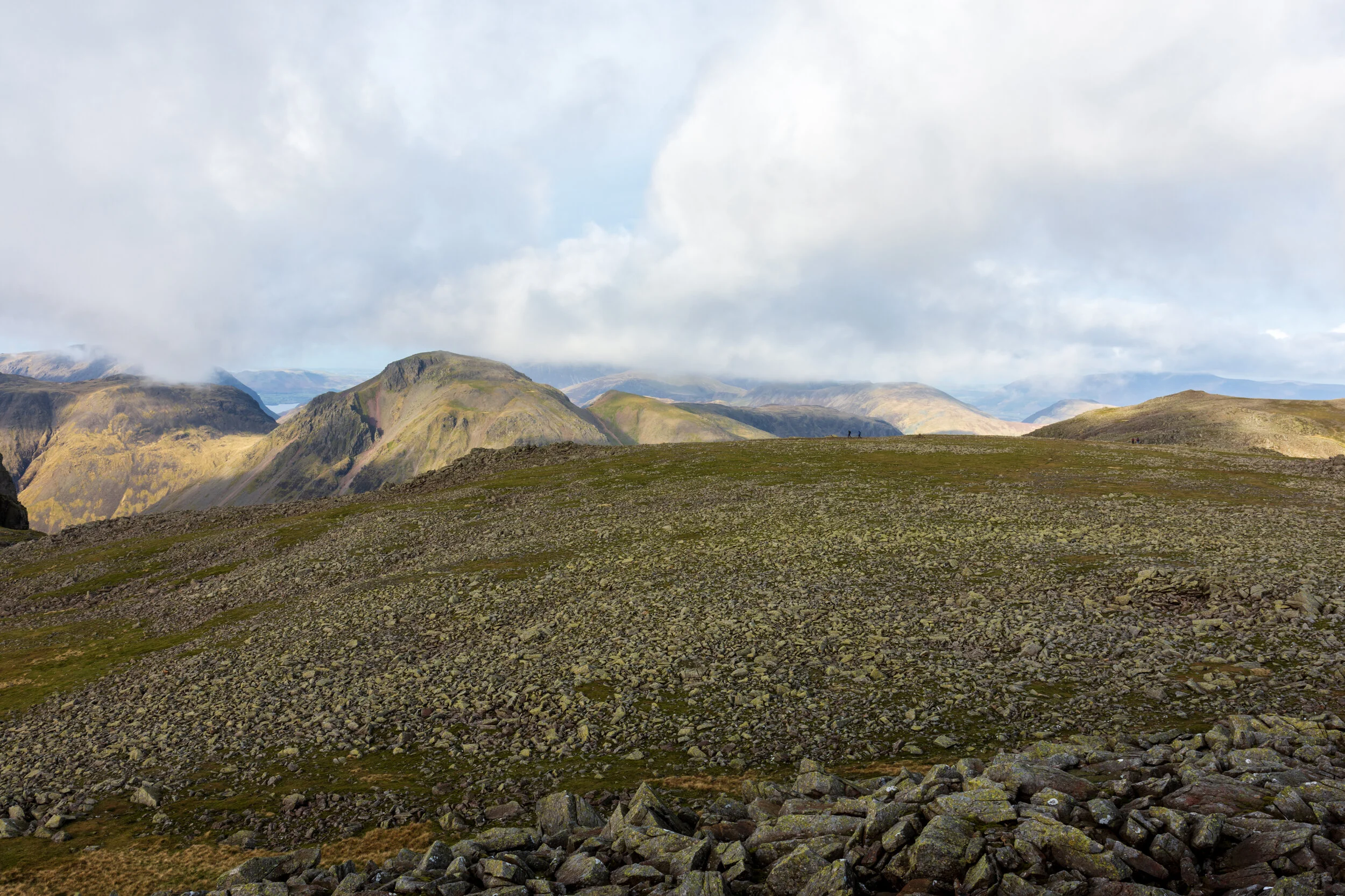 The view over the ‘rock field’ on Ill Crag summit, a rocky, desolate landscape with several large mountains in the background, towering into the clouds