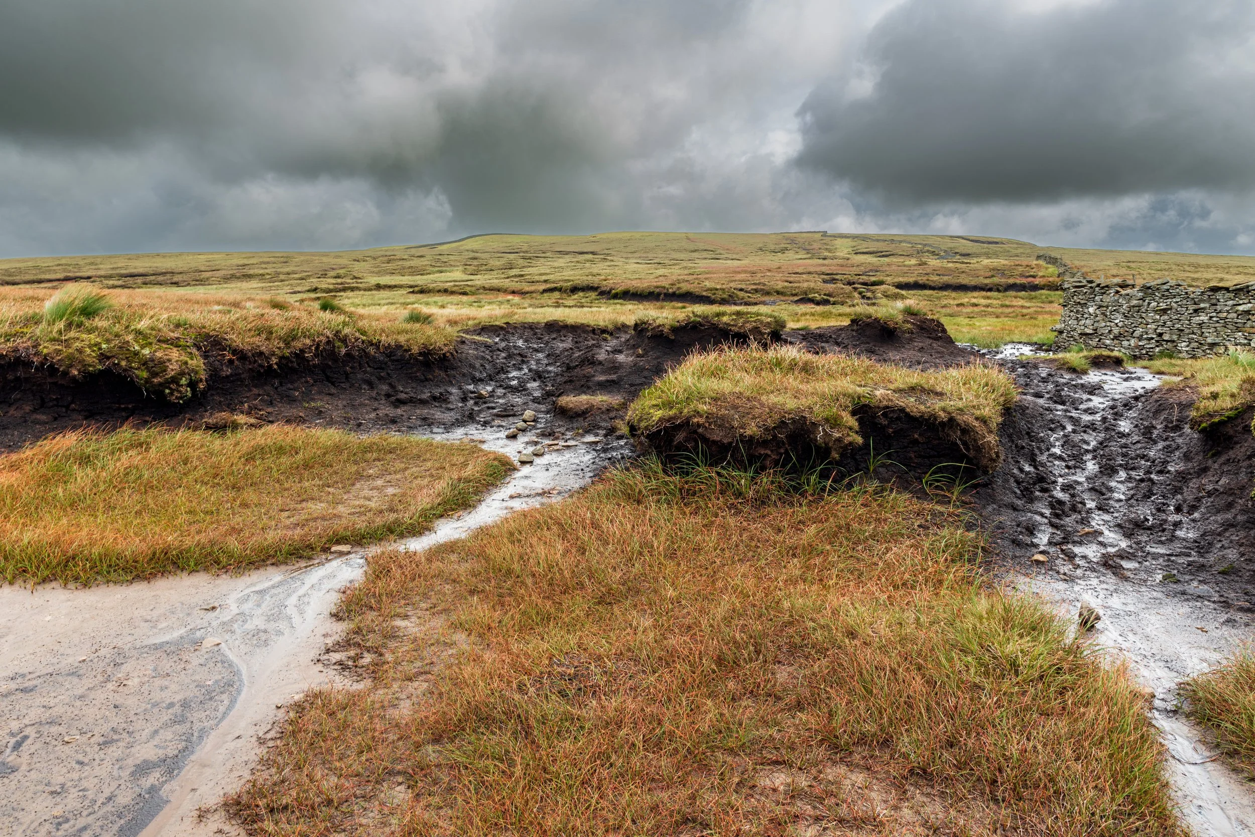 Boggy peat hags on the approach to the summit of Plover Hill in the Yorkshire Dales, under a cloudy, stormy sky