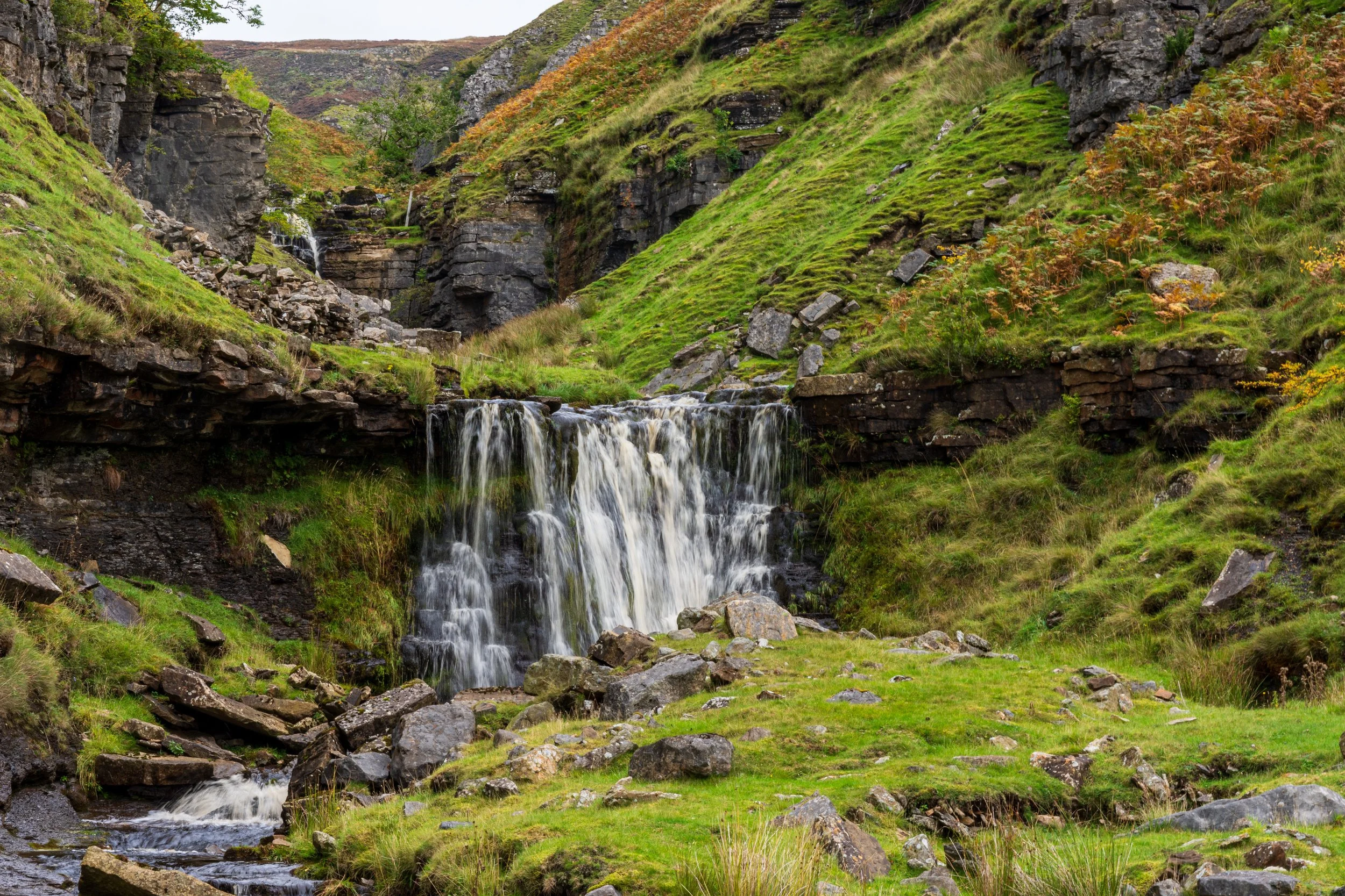 A softly flowing waterfall in Swinner Gill, on a wet day, with Rogan's Seat in the background.