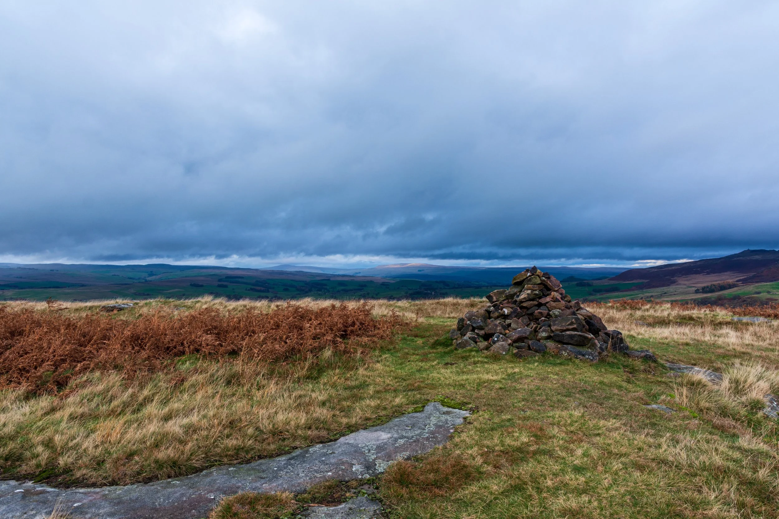 A cairn on top of the summit of Rough Haw in the Yorkshire Dales, looking out towards Buckden Pike and Great Whernside, under a stormy sky