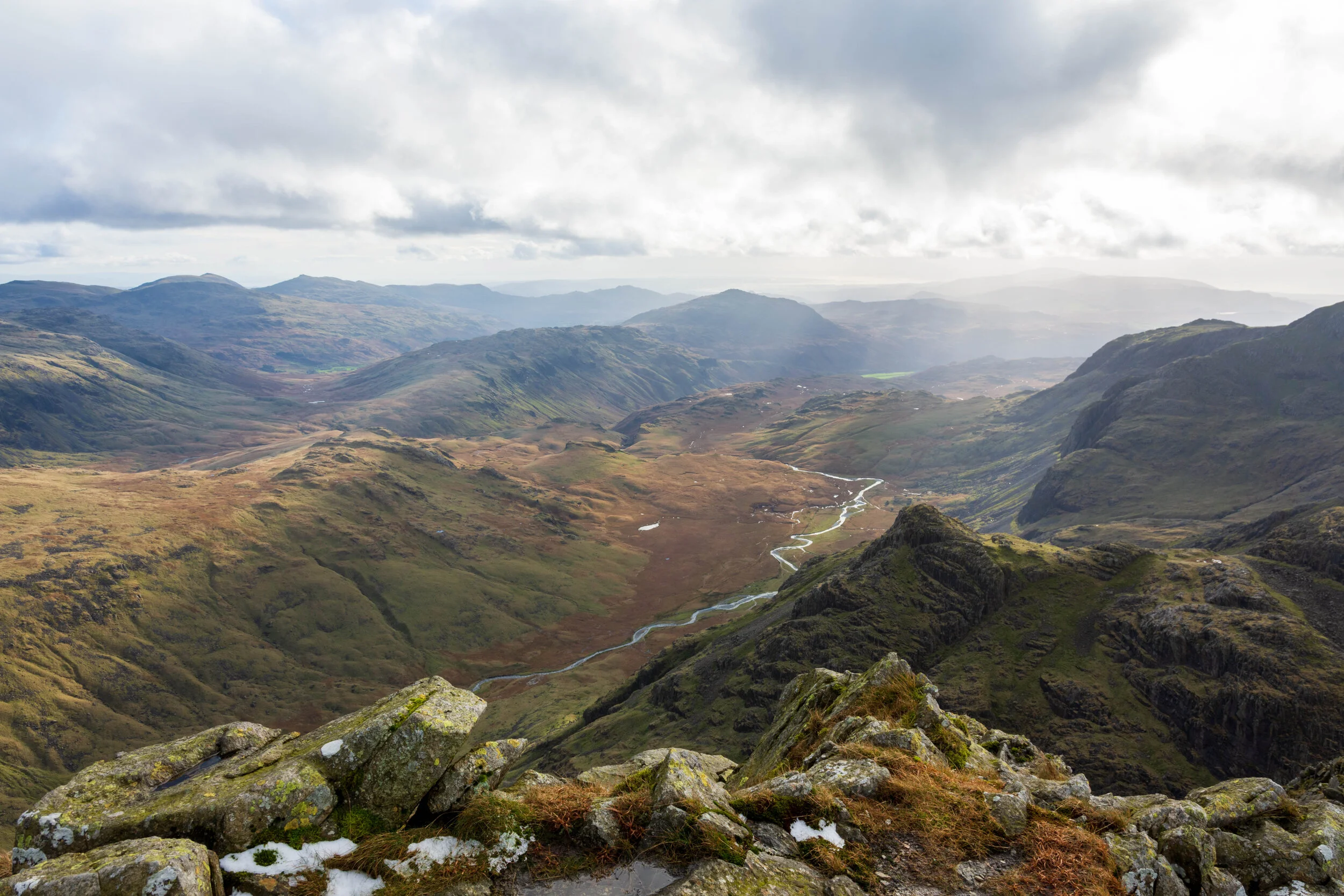 A view of Eskdale and the South Western Lake District from Ill Crag, near Scafell Pike. The River Esk snakes though the valley with Harter Fell in the background. Some snow and ice is on the foreground rocks