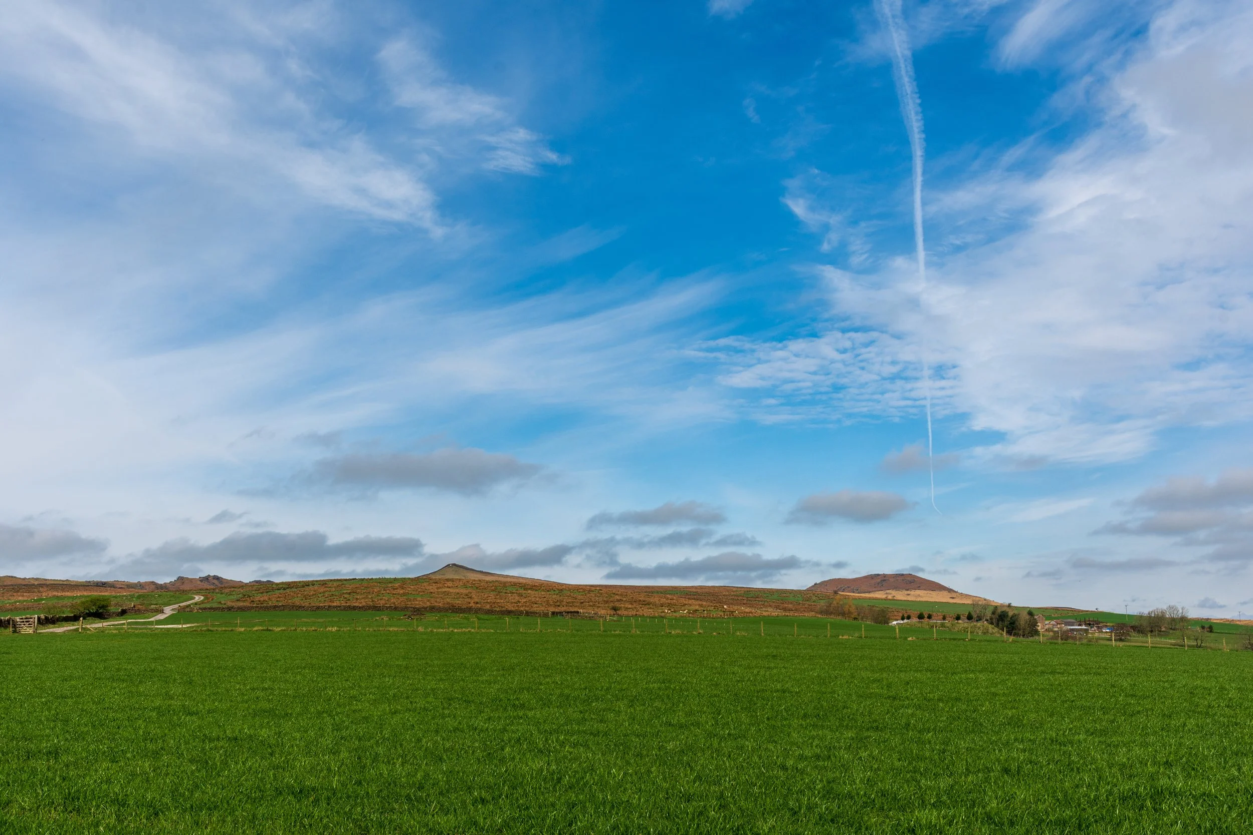 Sharp Haw hill in the Yorkshire Dales and Rough Haw viewed from a distance across a green farm field in the foreground and a blue sky