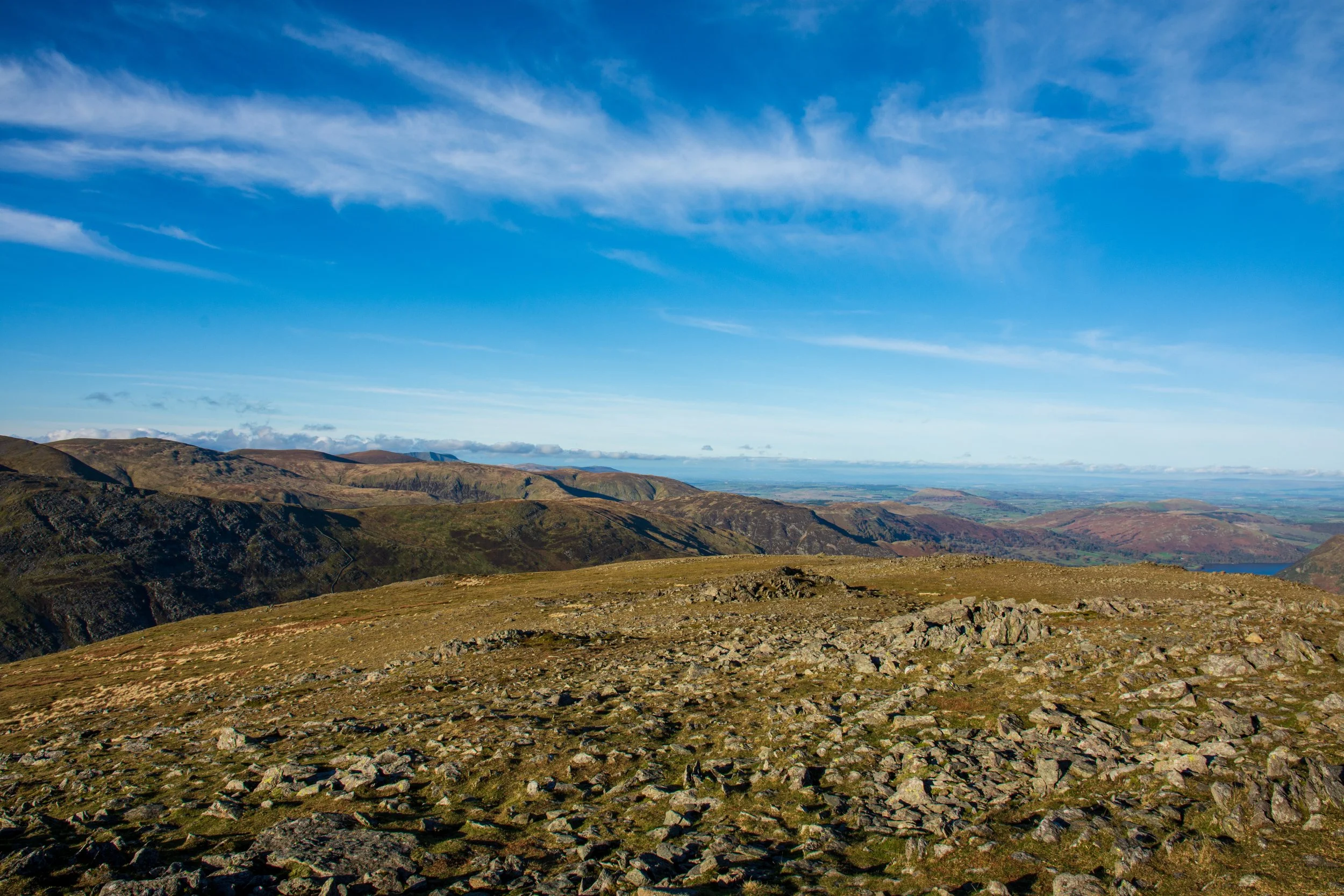 The rocky summit of St Sunday Crag in the Lake District, looking east towards Sheffield Pike and Ullswater, on a clear day under a blue sky