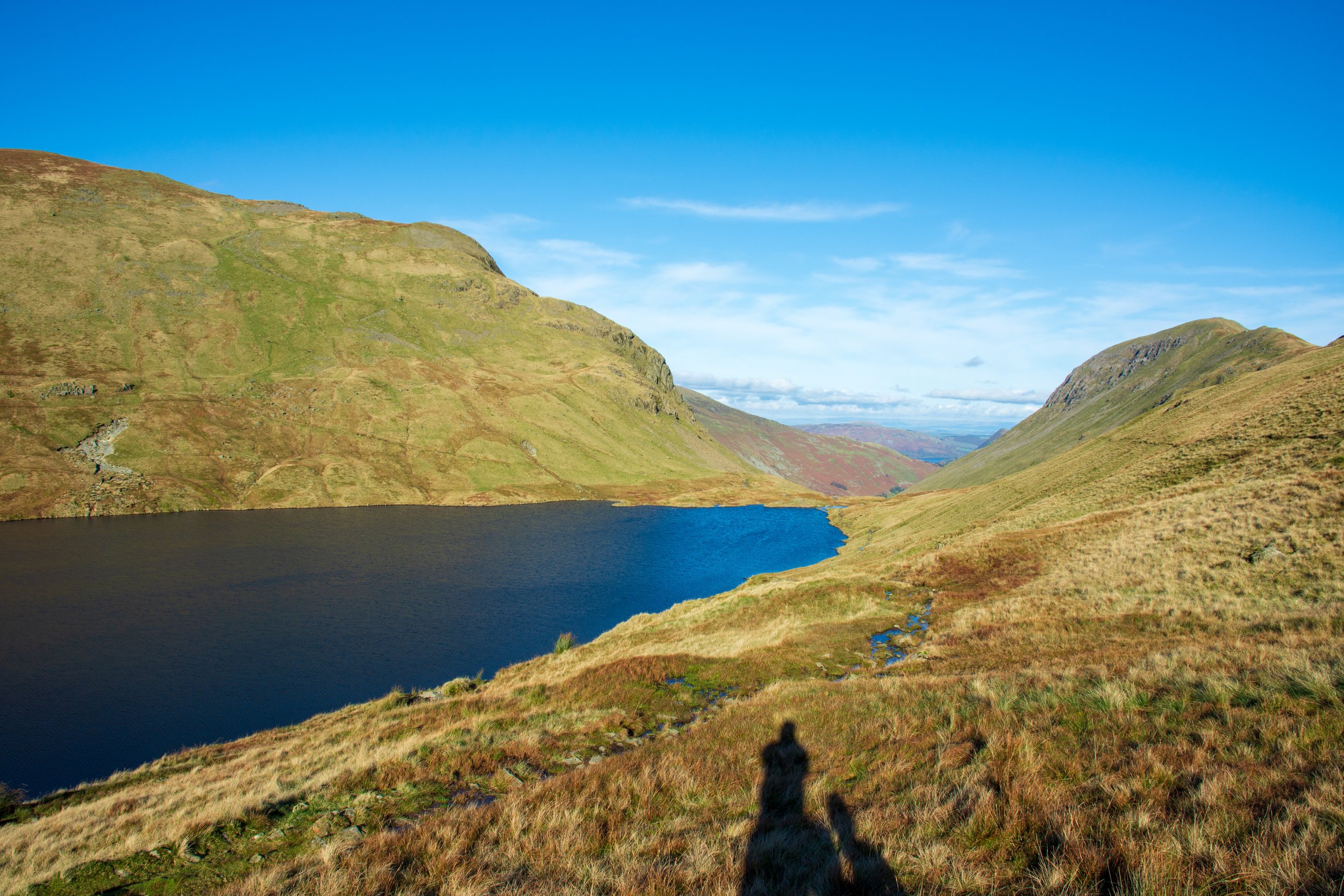 Griesdale Tarn in the Lake District on a clear, sunny day, under a blue sky, with the mountain of St Sunday crag on the right and Dollywagon Pike on the left