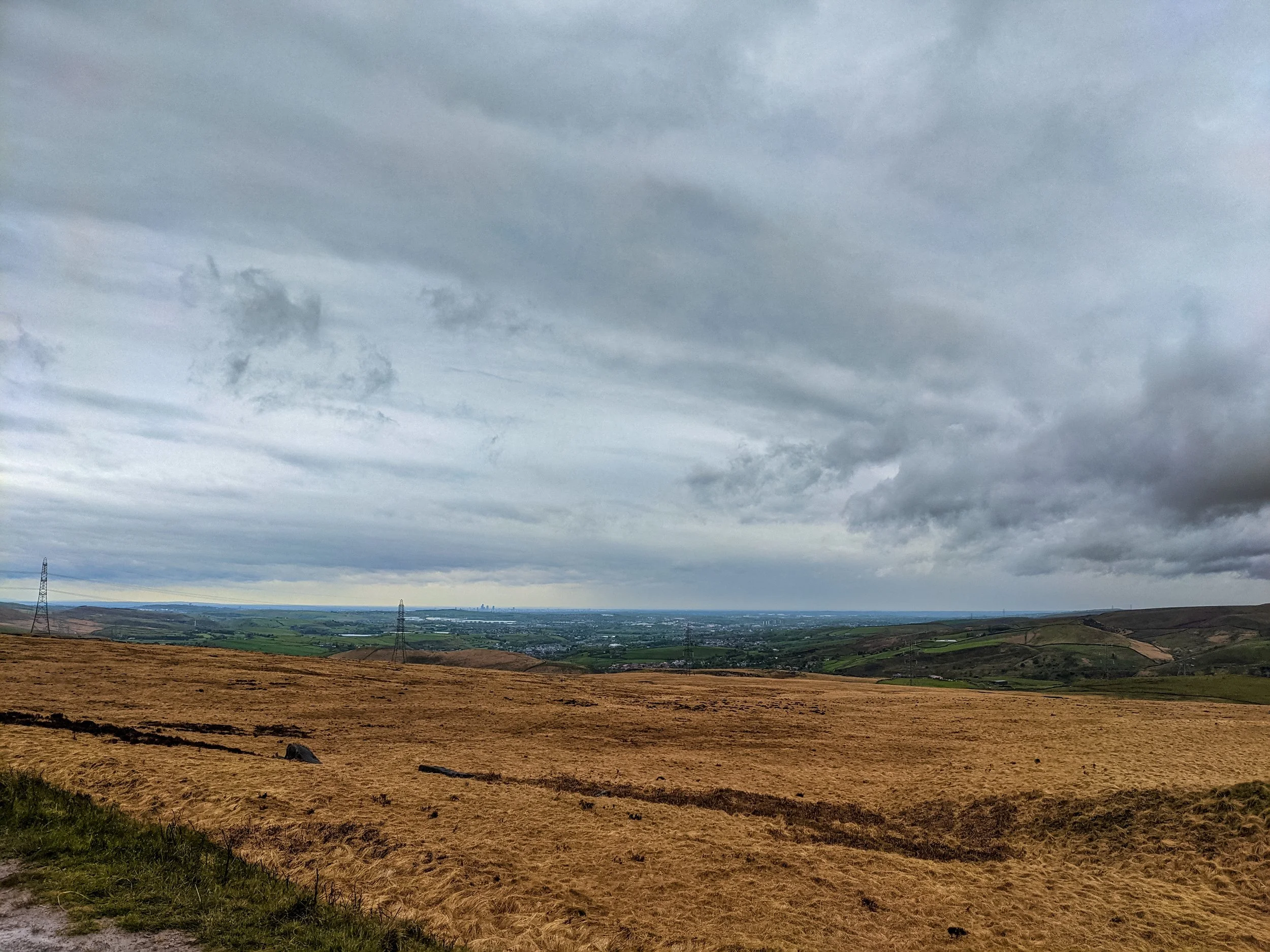 A view of Manchester from Stoodley Pike, with desolate moorland in the foreground, and under a cloud sky