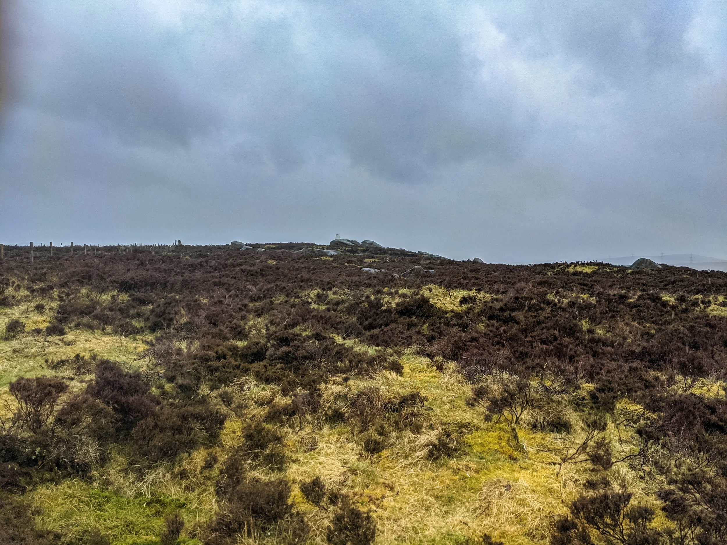 A trig point near Stoodley Pike, on a heather moor, under a rainy sky