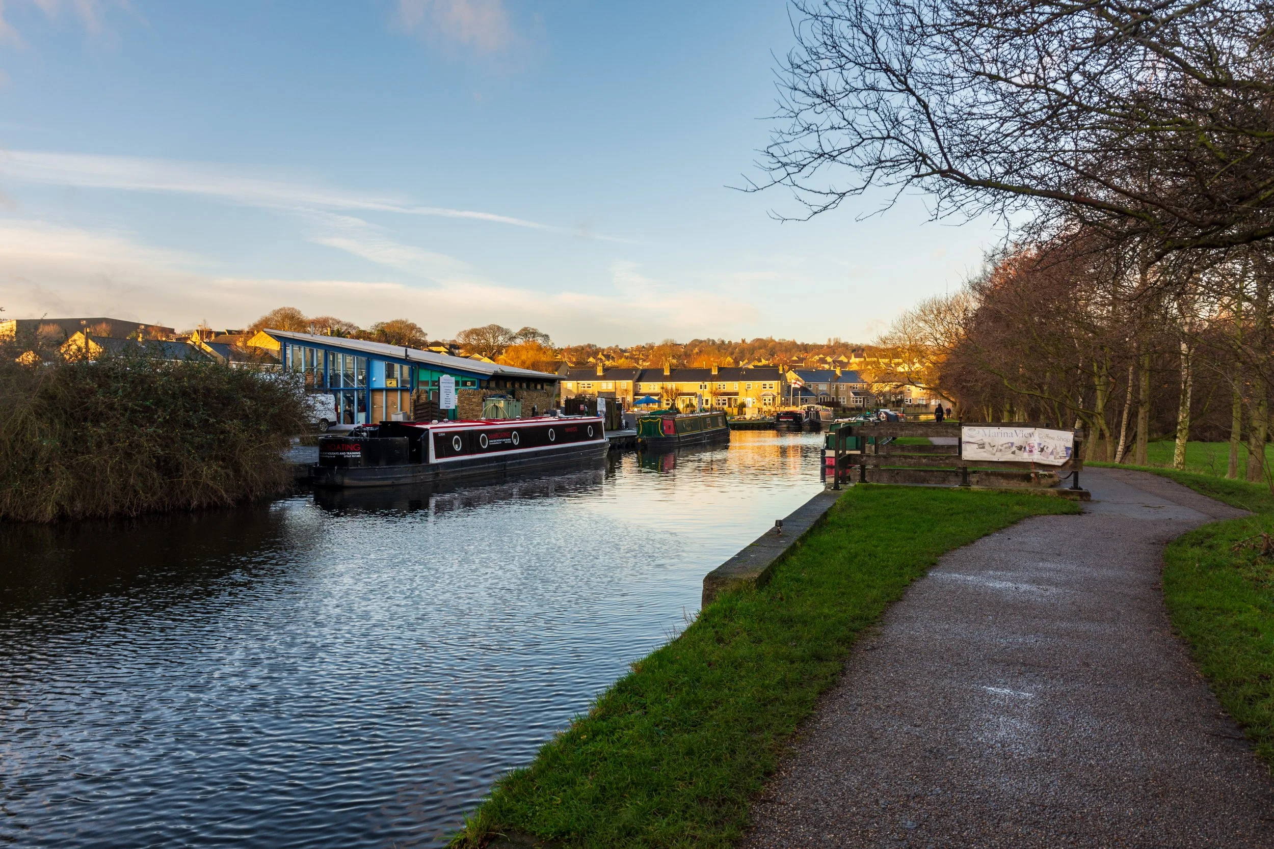 Canal long boats or barges, moored on the side of a canal next to a marina, on a beautiful winter's morning, with a clear sky, on the Leeds-Liverpool canal at Apperley Bridge