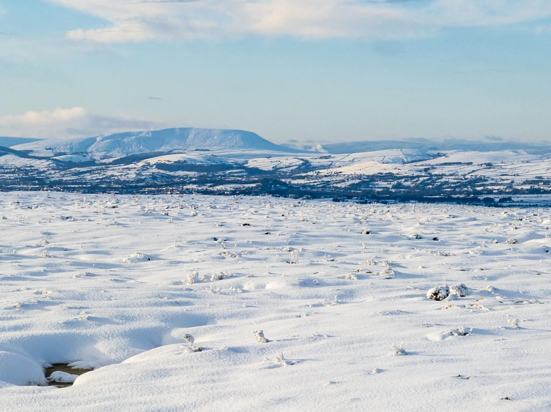 A snowy moor near Wolf Stones, looking towards a snow-covered Pendle Hill, on a sunny winter afternoon