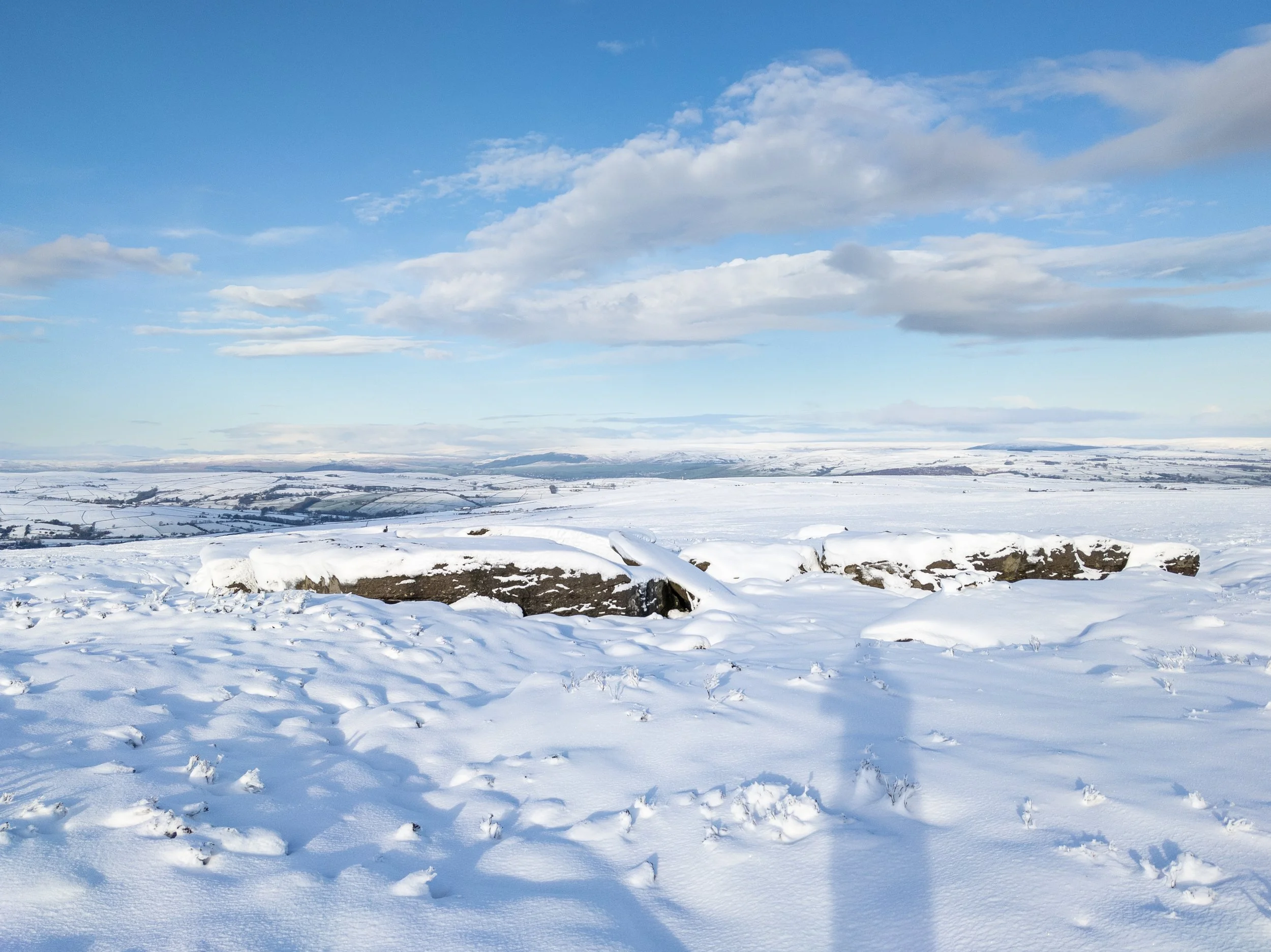 The snow-covered Maw Stones on a sunny winter day, looking over the snowy moors towards Skipton, against a blue sky
