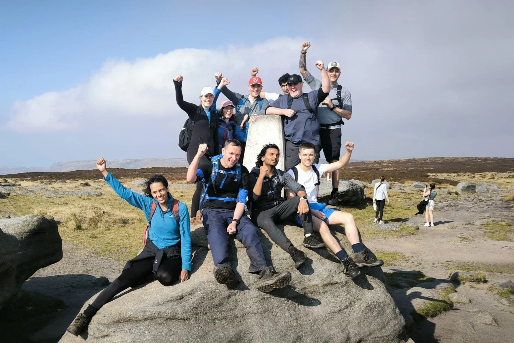A corporate group taking on a Charity Challenge Hike (Derbyshire Three Peaks), celebrating at the trig point at Kinder Low on Kinder Scout in the Peak District