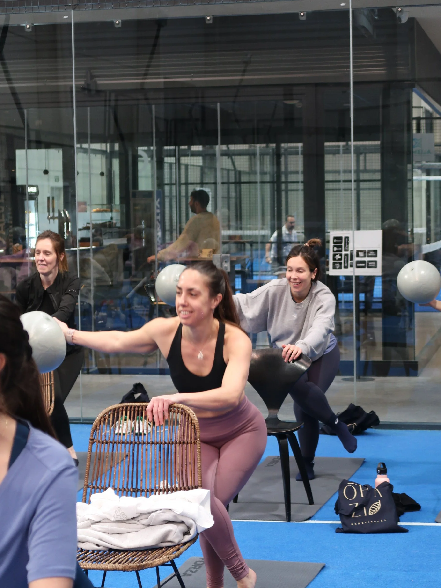 OHAZI EXPERIENCES: grupo de mujeres participando en una clase de ejercicio en un gimnasio, realizando estiramientos con pesas en las manos