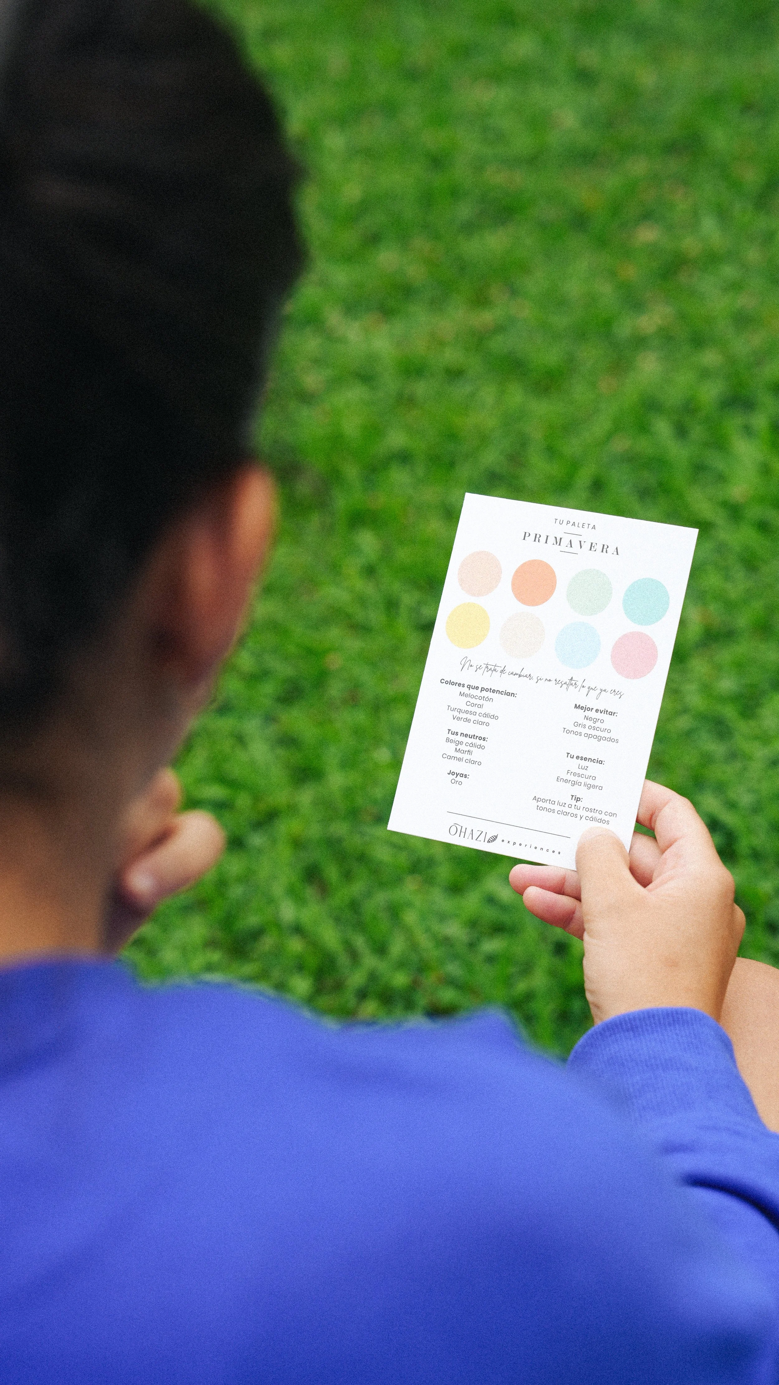 Persona sosteniendo una tarjeta con paleta de colores de primavera, texto y consejos de belleza en un ambiente al aire libre con césped.