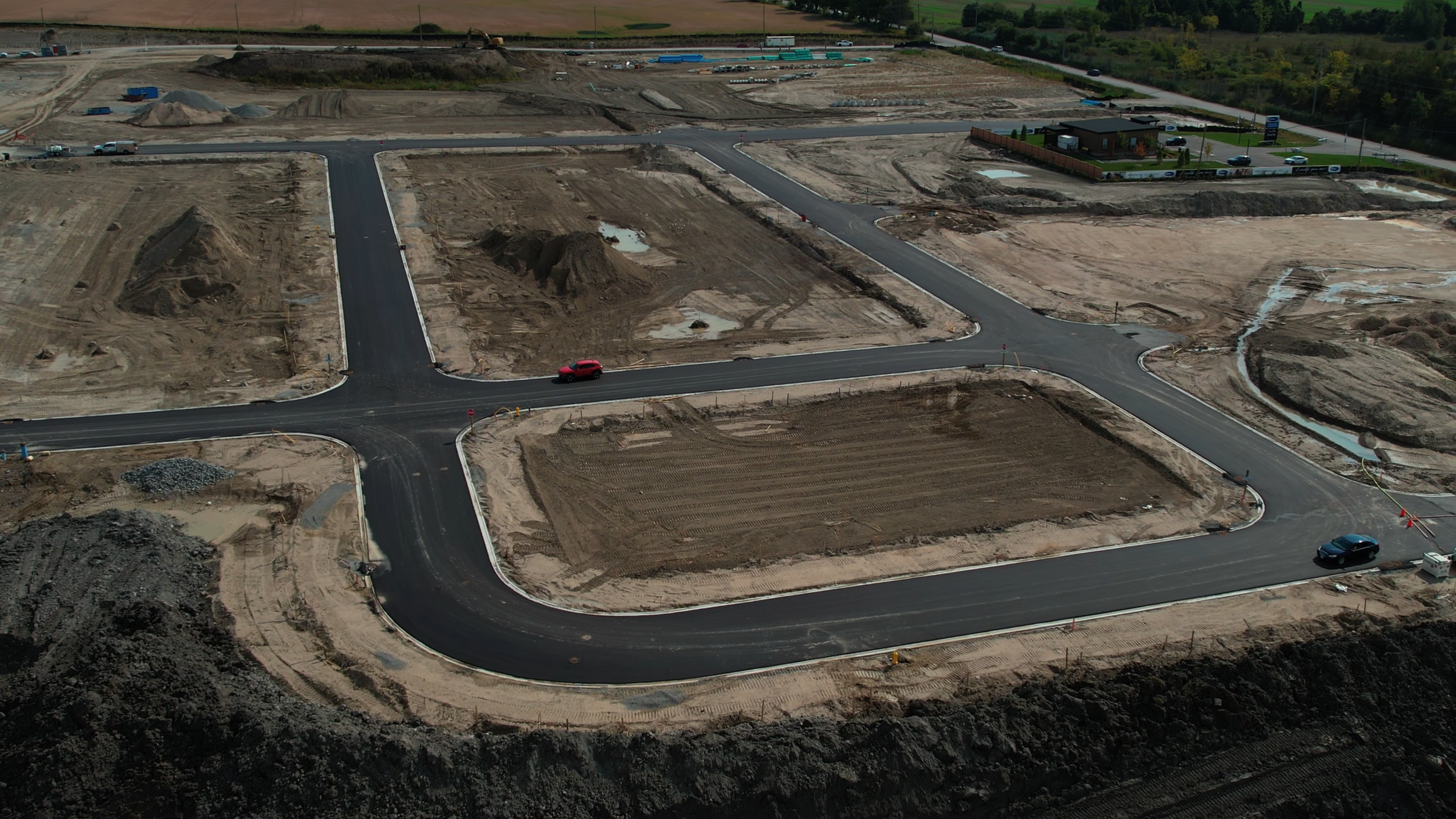 Aerial view of a construction site with newly paved roads, some dirt and gravel, and a few cars driving on the roads.
