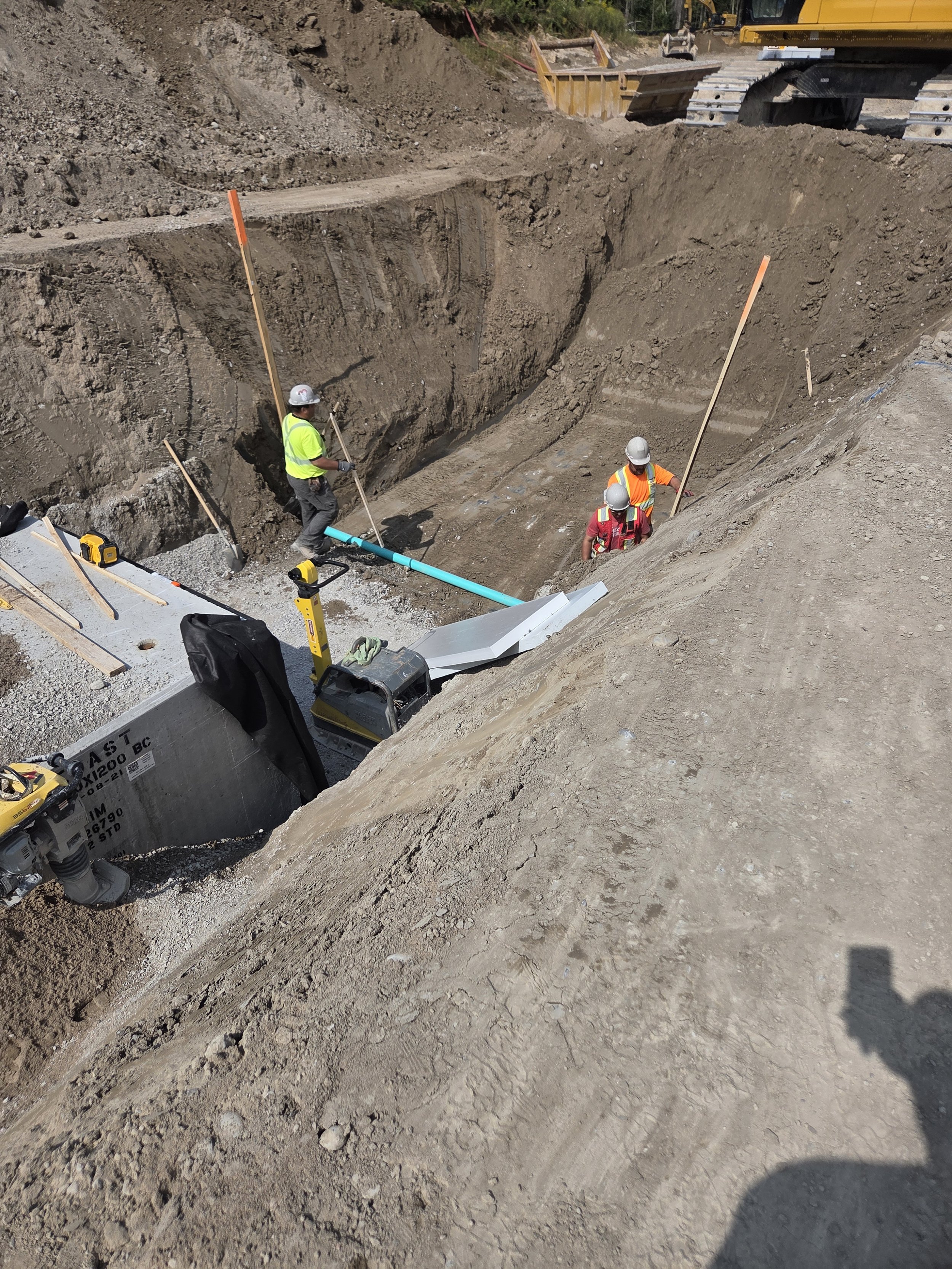 Construction workers in safety gear excavating a large trench at a construction site, with construction equipment and tools around.