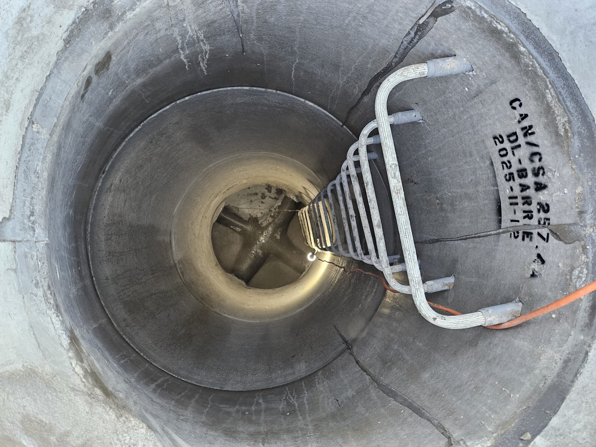 Inside of a manhole or inspection shaft showing a ladder and some electrical or communication cables.