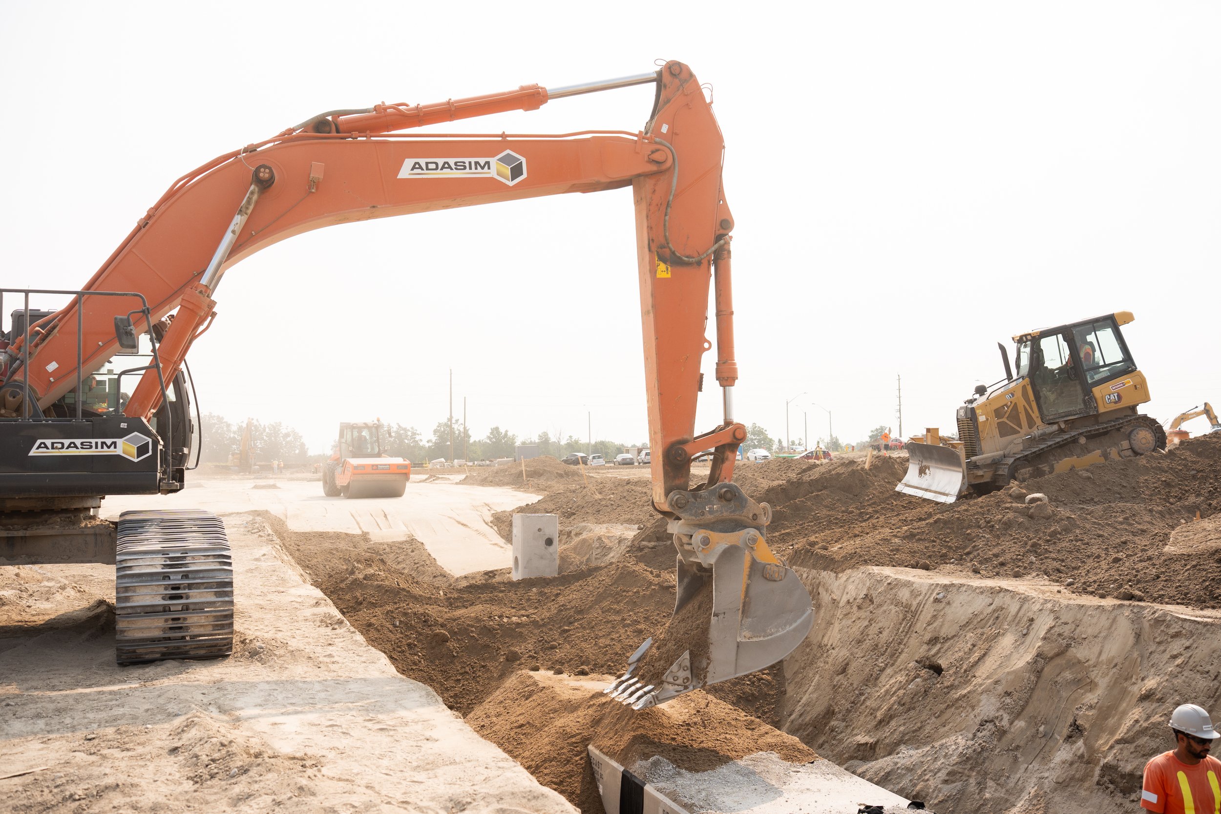 Construction site with excavator digging a trench and bulldozer moving dirt, workers wearing safety gear