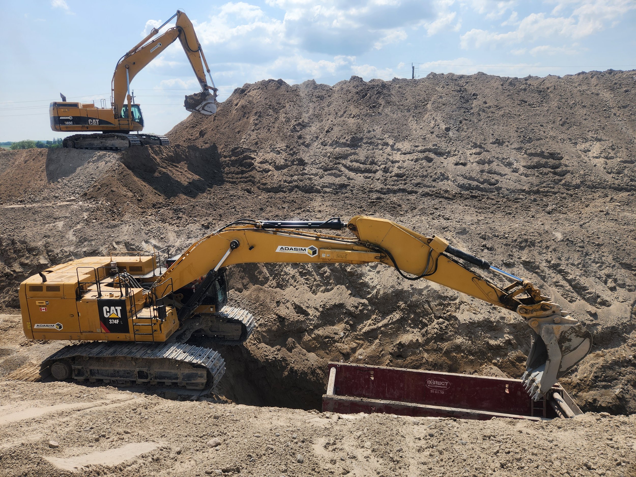 Two yellow Caterpillar excavators working on a dirt slope, with one digging and the other positioned on top of the slope.