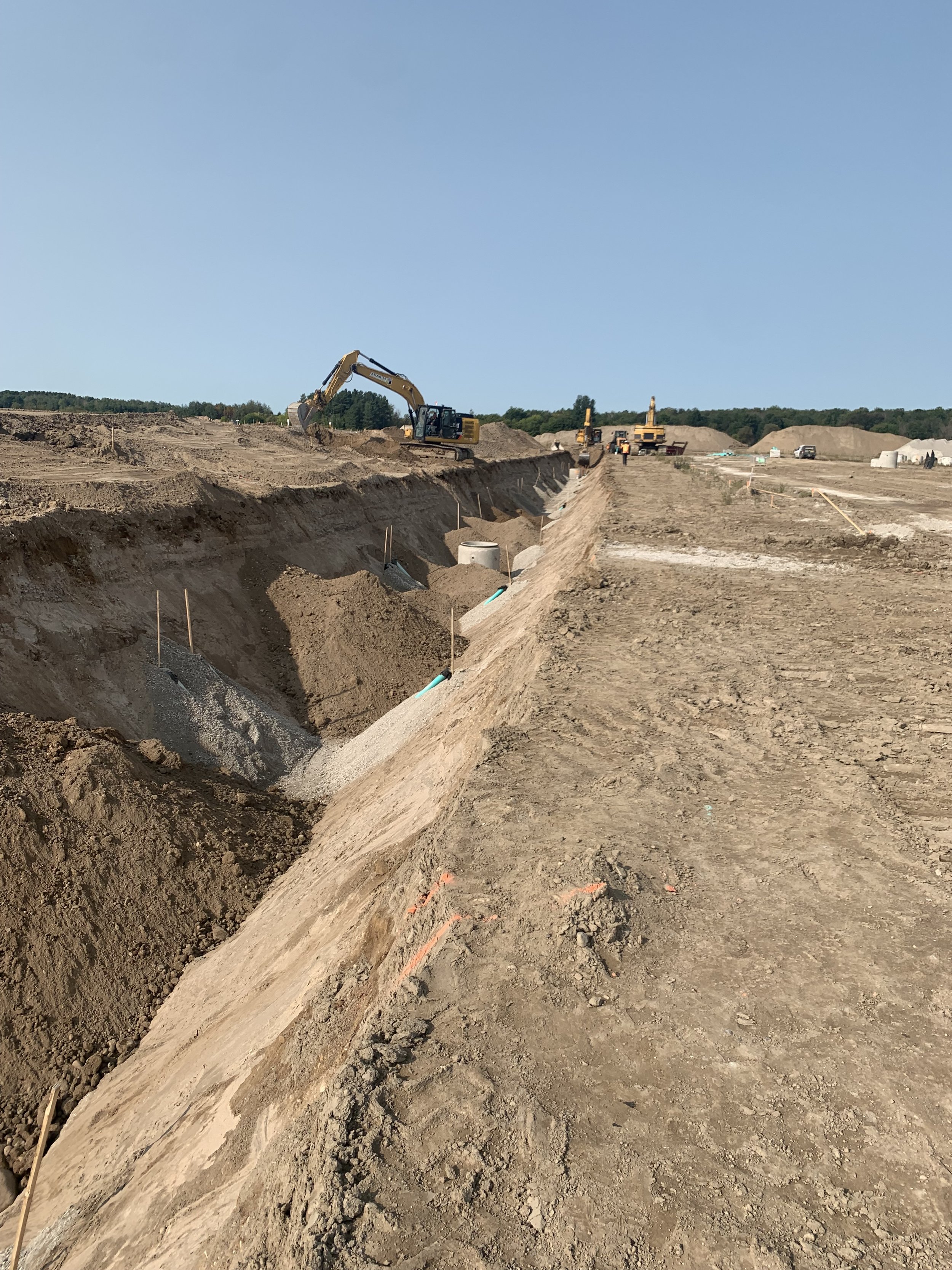 A construction site with excavators and bulldozers working on a large dirt trench, with blue sky in the background.