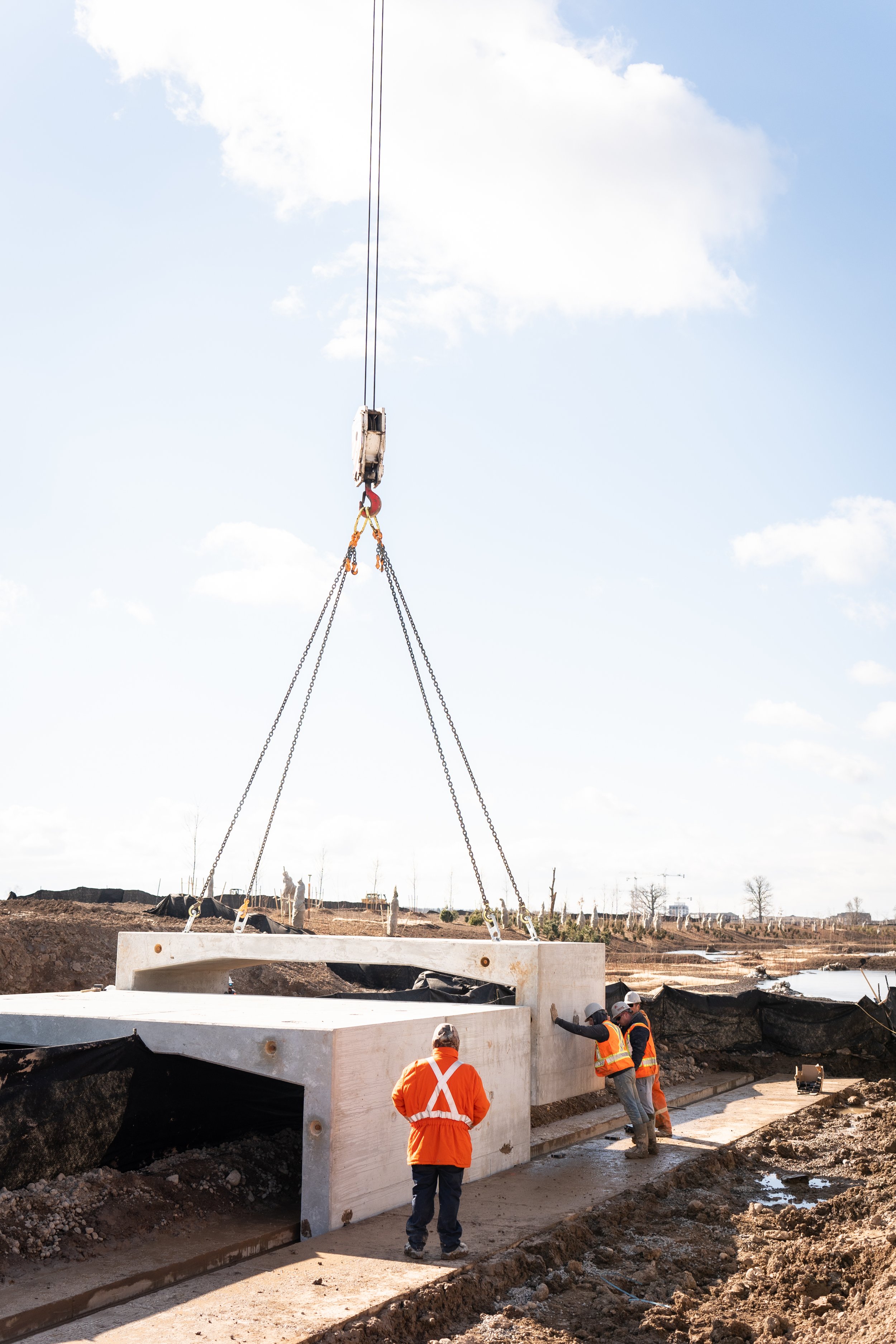 Construction workers in safety gear guiding a large concrete structure being lifted by a crane at a construction site.