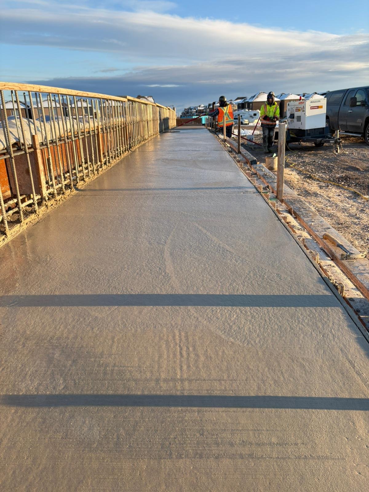 Workers pouring and smoothing concrete on a sidewalk in a neighborhood.