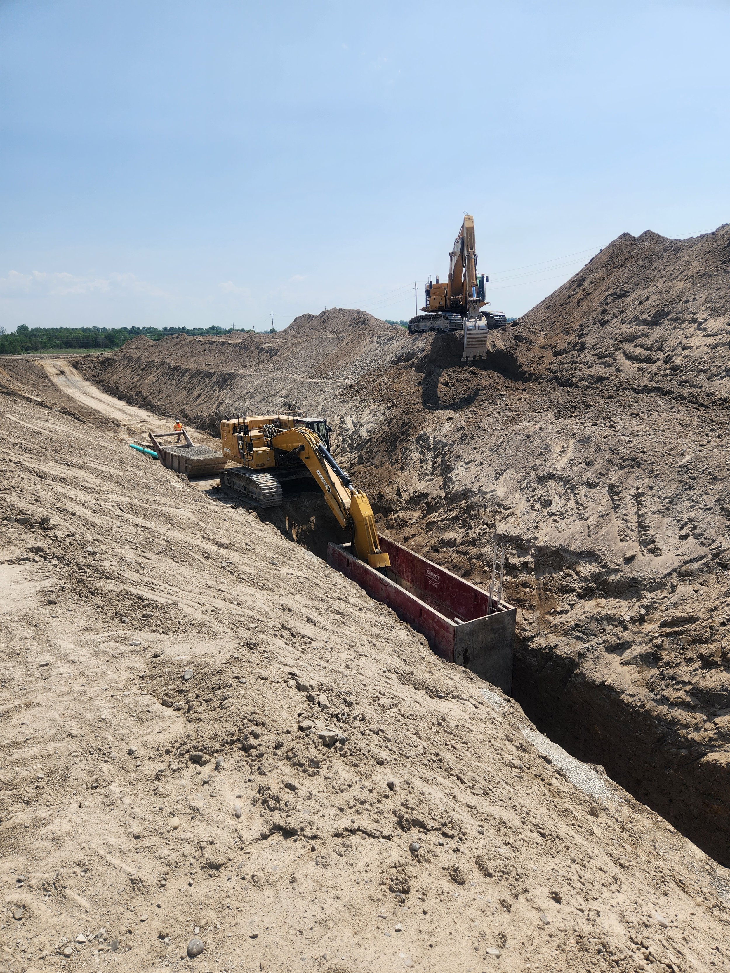 Construction site with two yellow excavators working on a deep trench, digging and moving dirt on a sunny day.