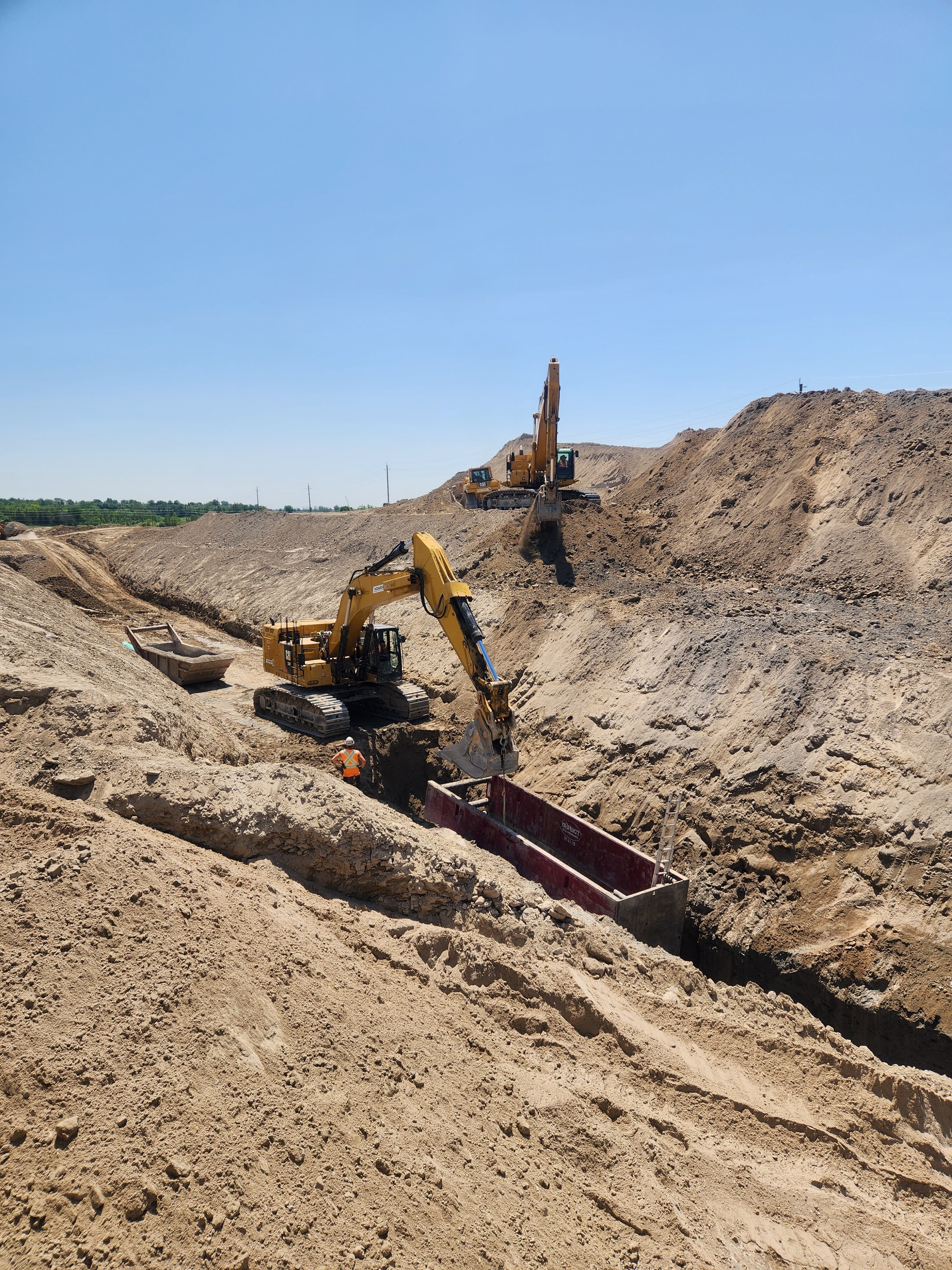 Construction site with multiple excavators working in sandy terrain under clear blue sky.