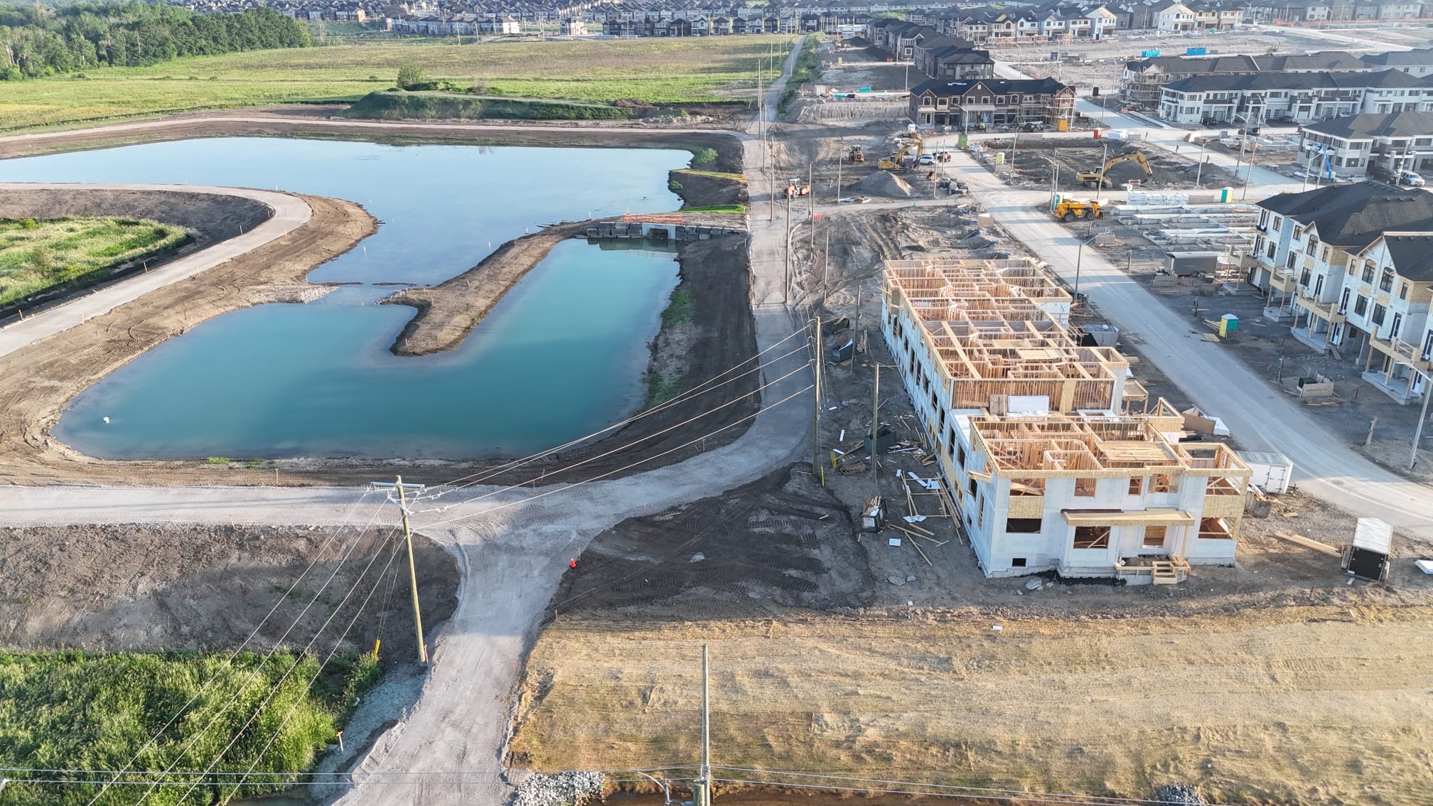 Construction site with a multi-story building under construction near two small ponds and a residential area in the background.