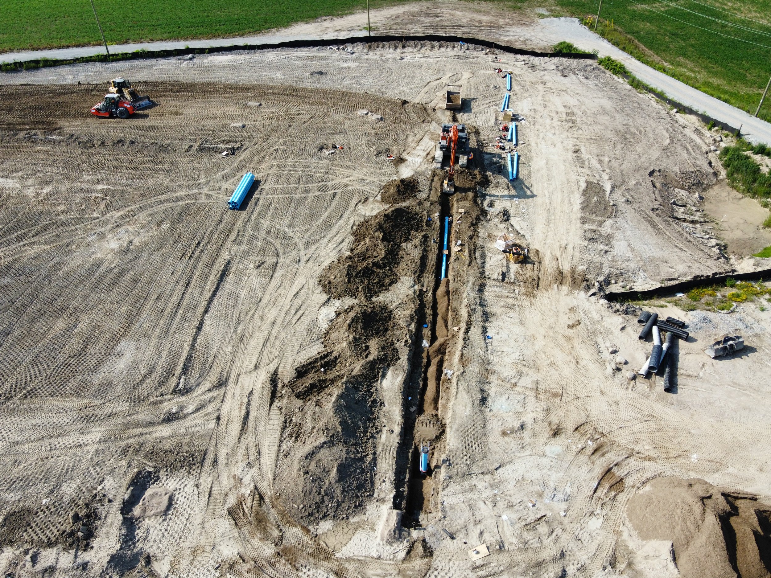 Construction site with dirt, machinery, and blue pipes being installed.