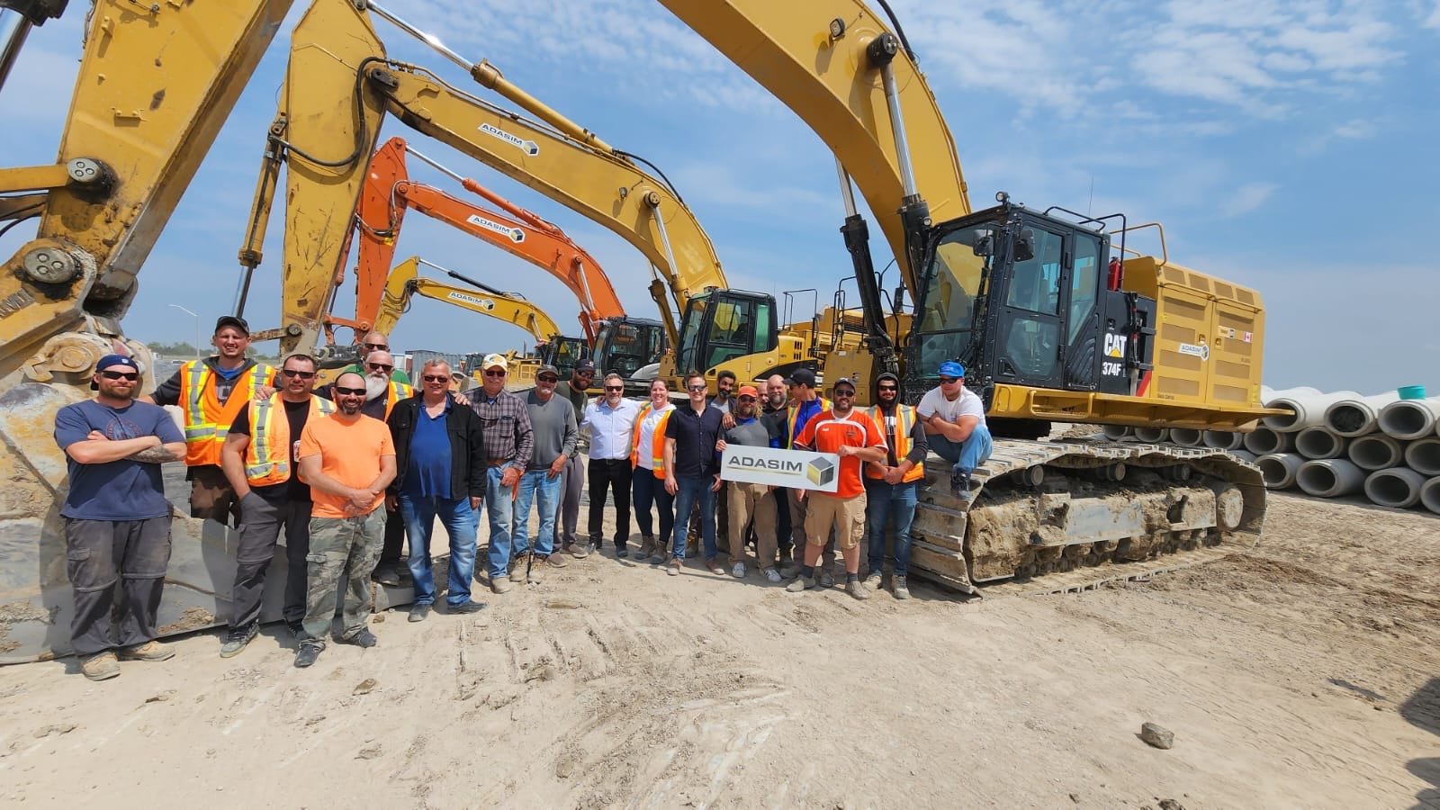 Group of construction workers and engineers standing in front of large excavators on a construction site, holding a sign that says 'ADASIM'.