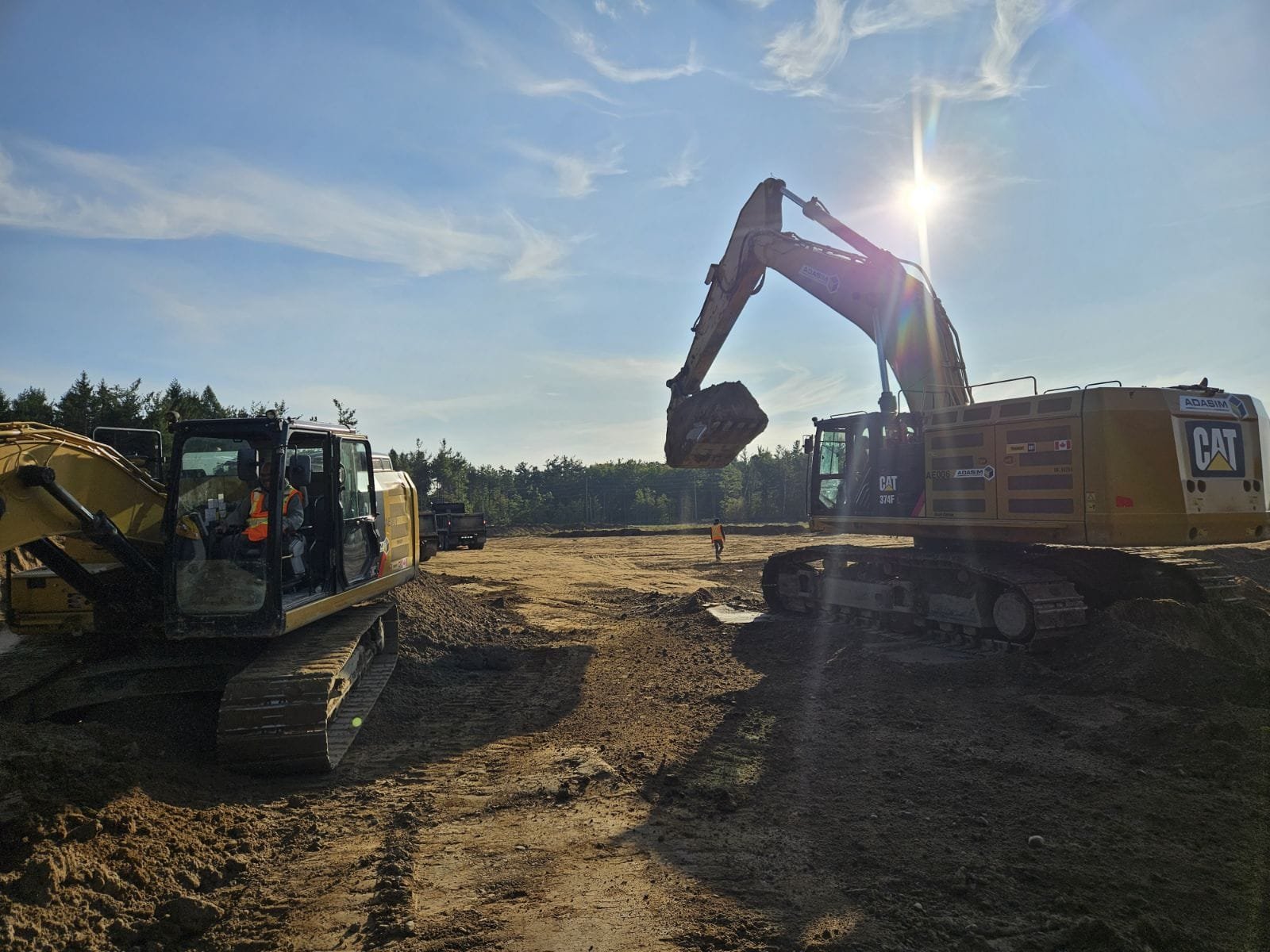 Construction site with two excavators working on dirt ground during daytime under clear sky with sunlight.