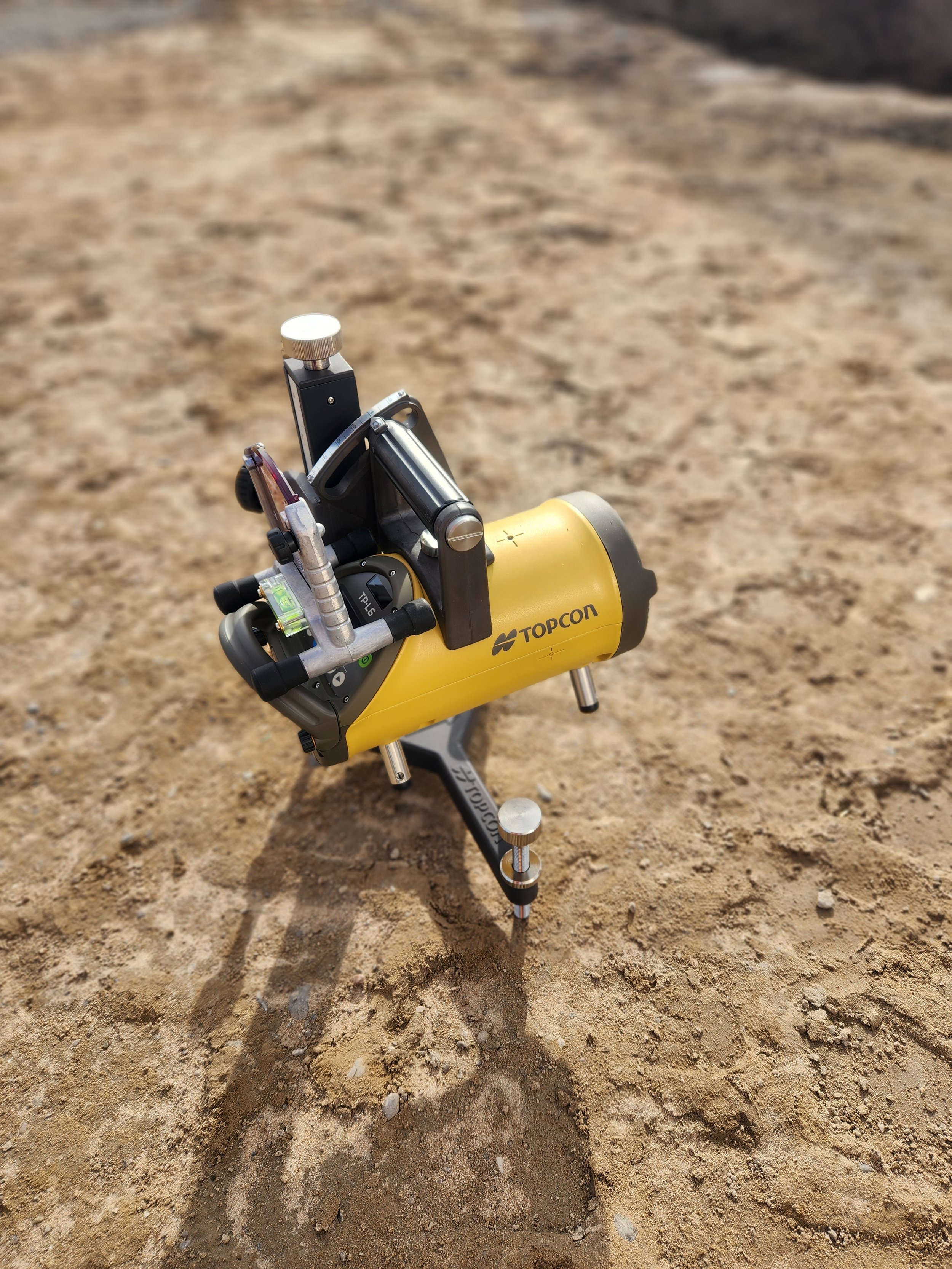 Surveying instrument, specifically a prism pole, placed on sandy ground in an outdoor setting.