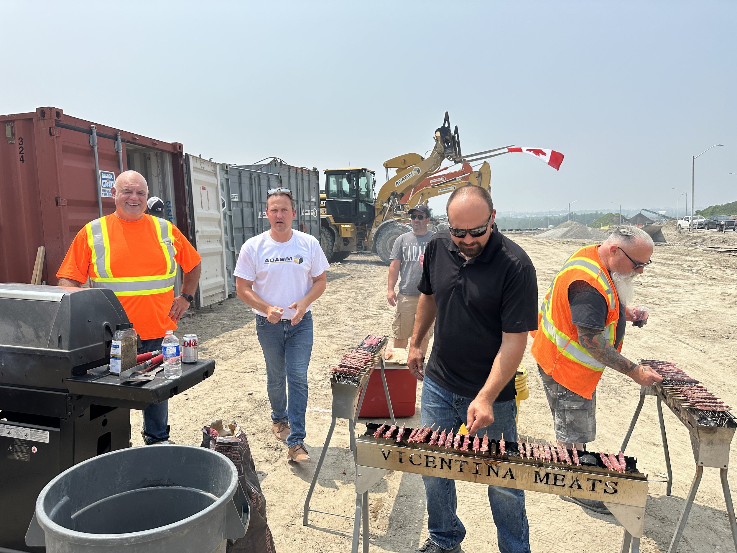 Group of men cooking skewered meat on barbecue grill at construction site.