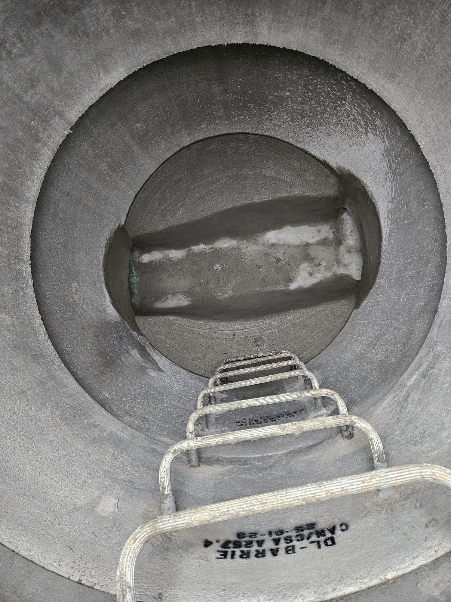 Inside a large concrete sewer pipe with a metal ladder leading down into it.