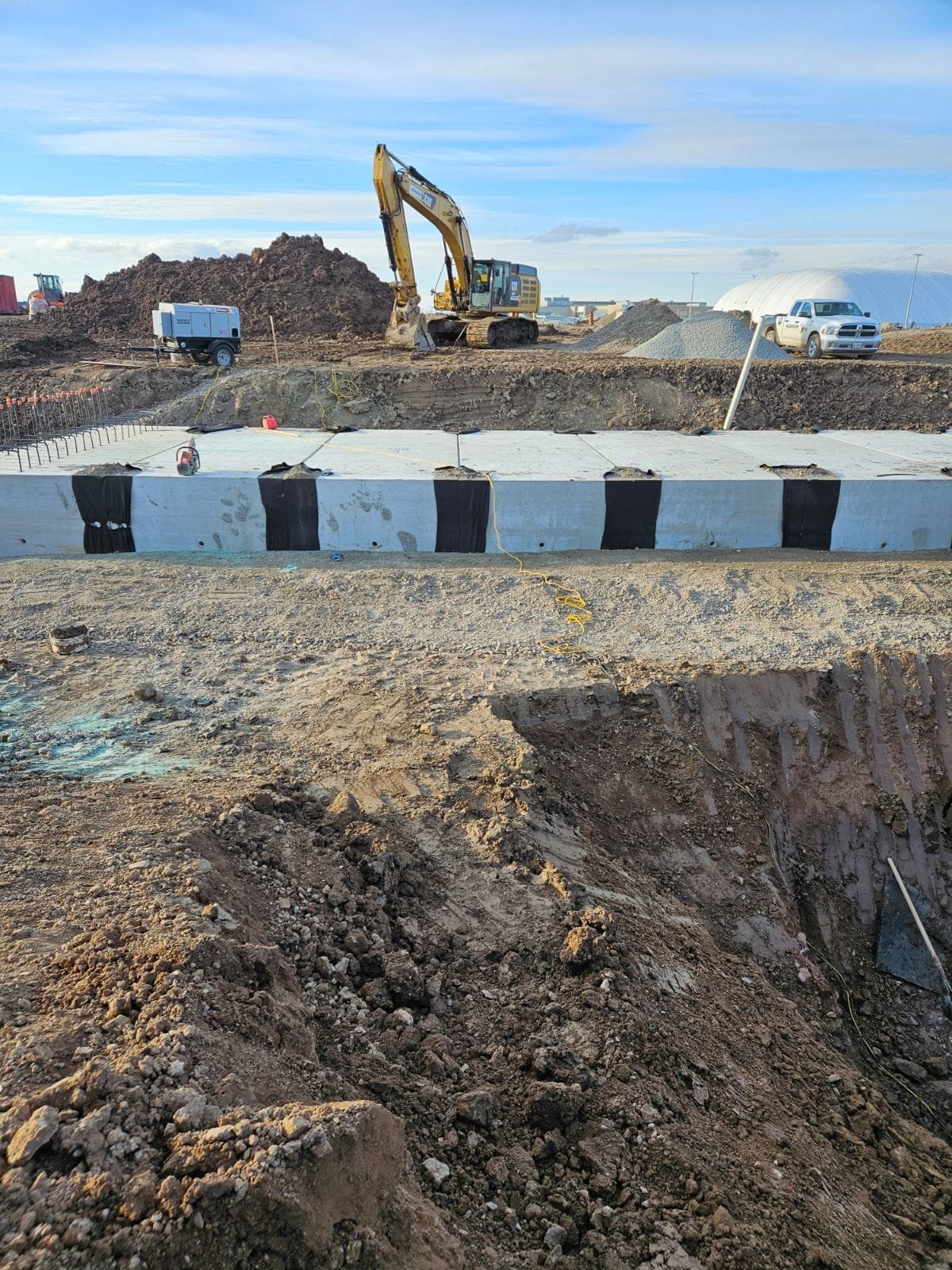 Construction site with excavator, trucks, and a concrete foundation being built.