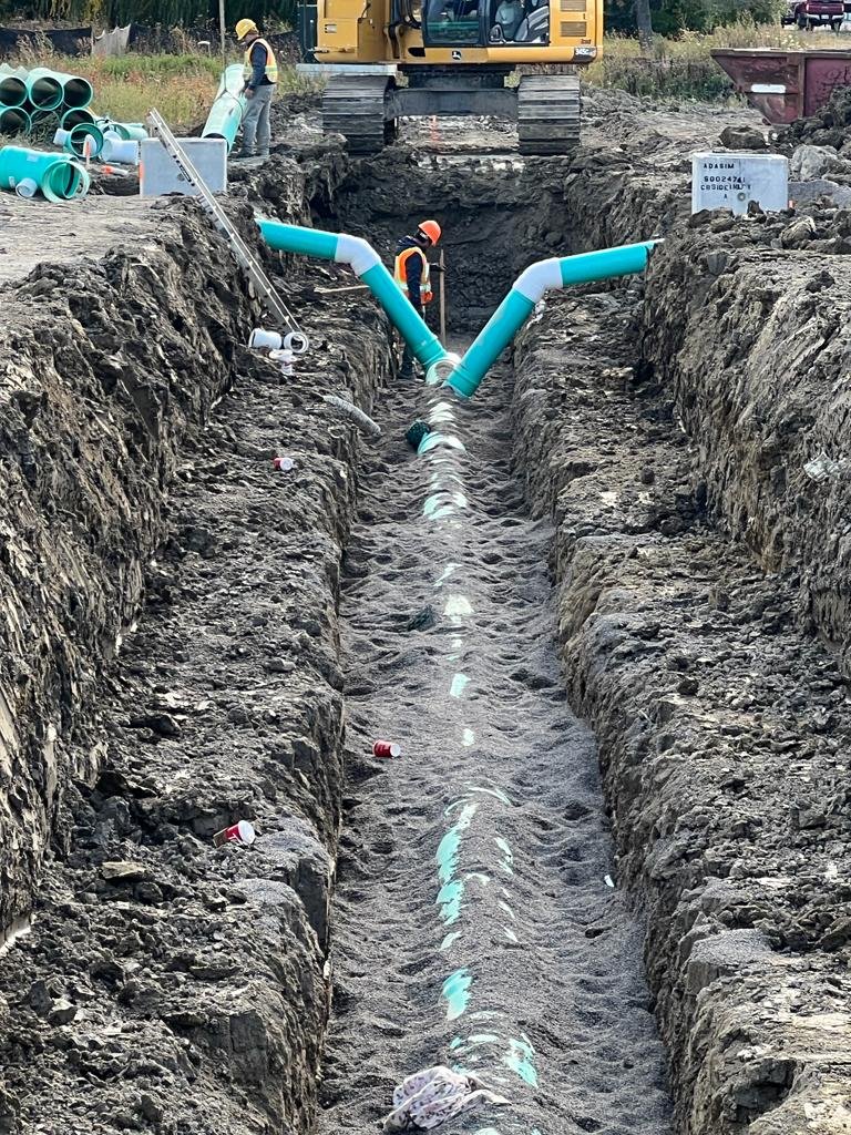 Workers installing large blue pipelines underground with construction equipment and soil surrounding the trench.