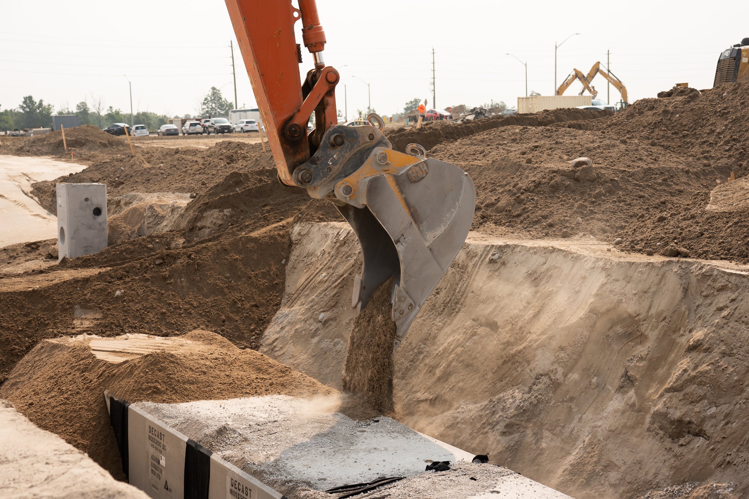 Construction excavator bucket scooping dirt into a trench at a construction site.