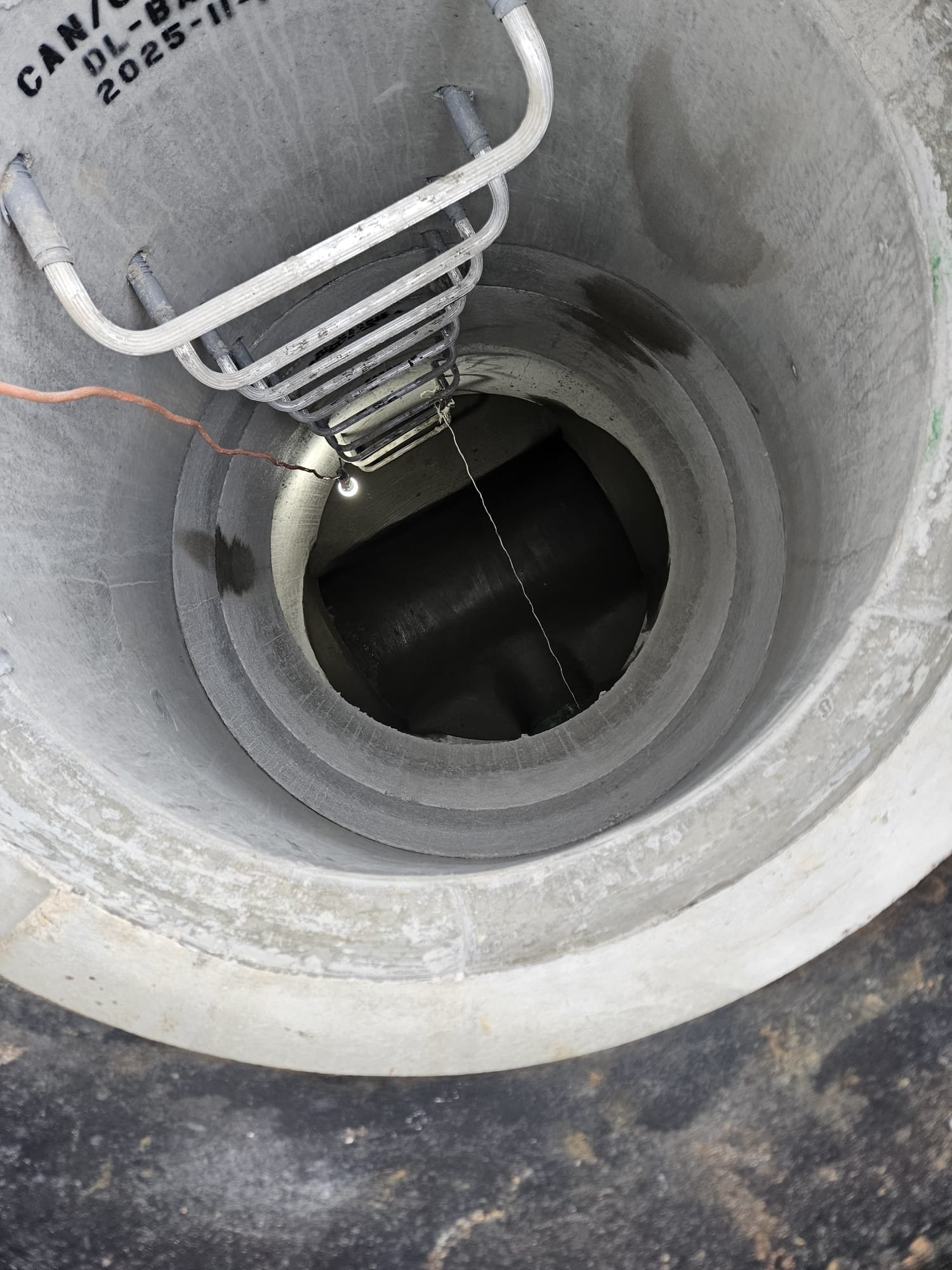 View looking down into an underground manhole or conduit with electrical cables and equipment inside.