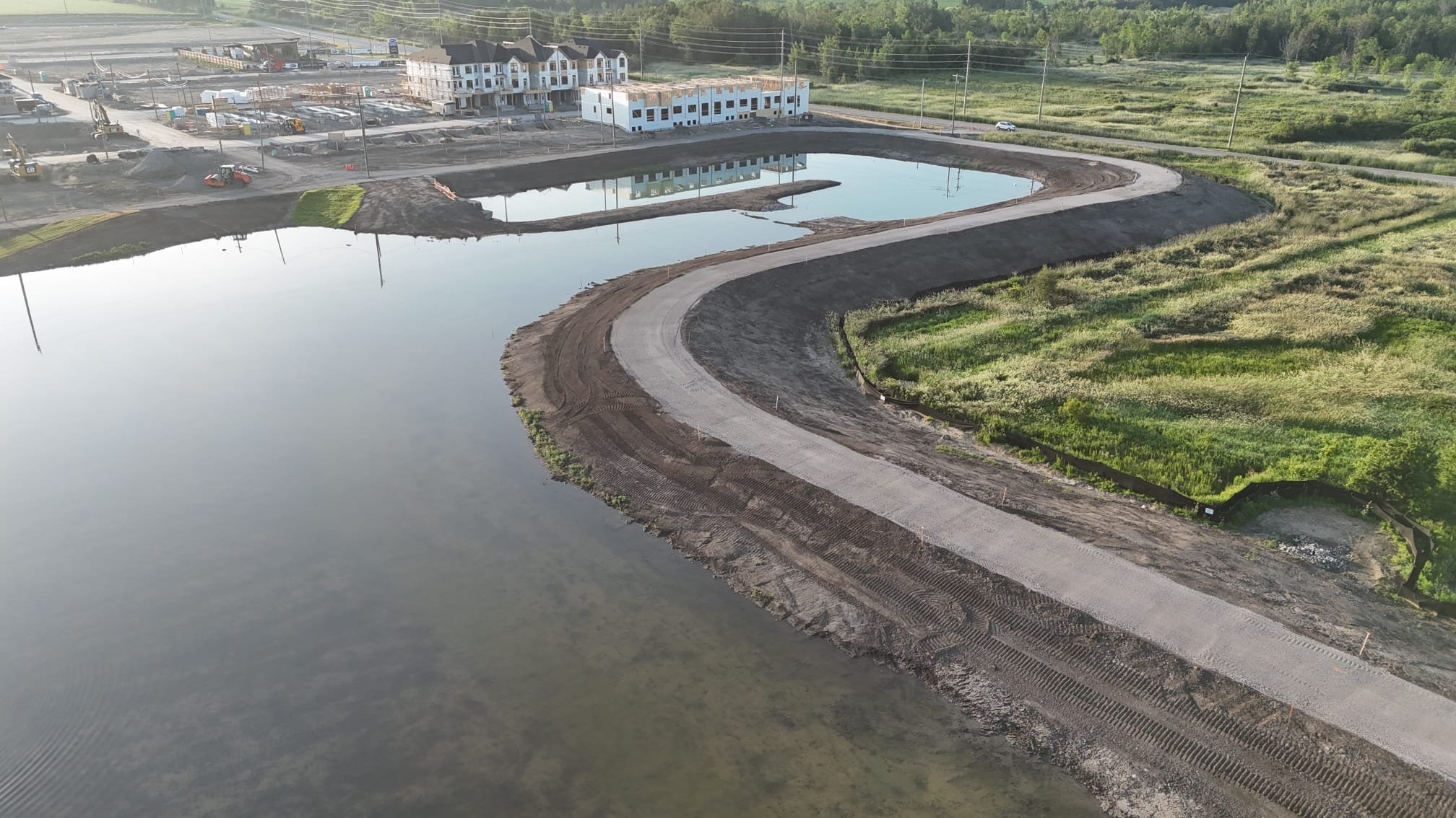 Construction site with a partially built road winding along a body of water, and a residential building under construction in the background.