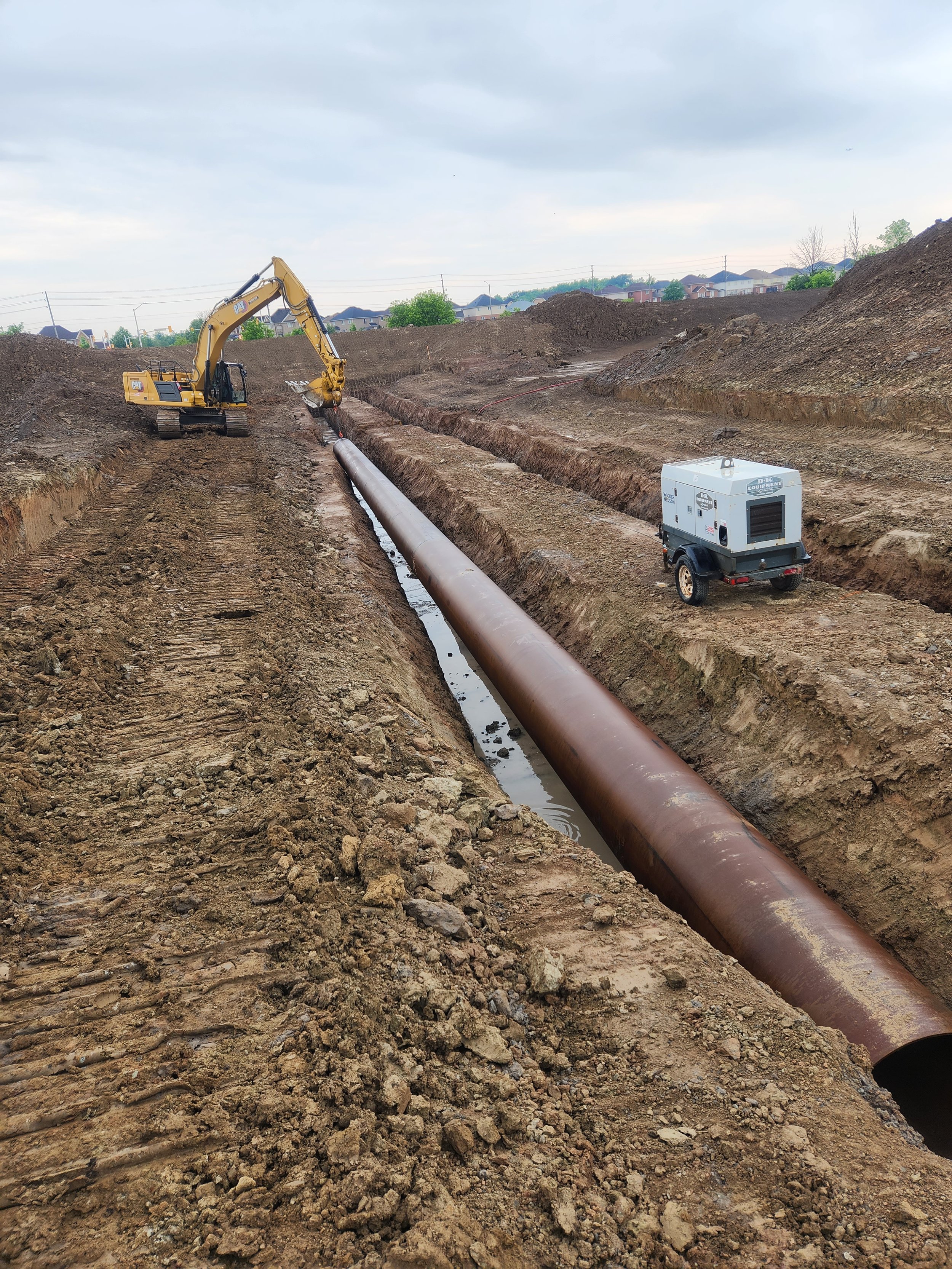 Construction site with excavator working on large pipeline in a dirt trench.