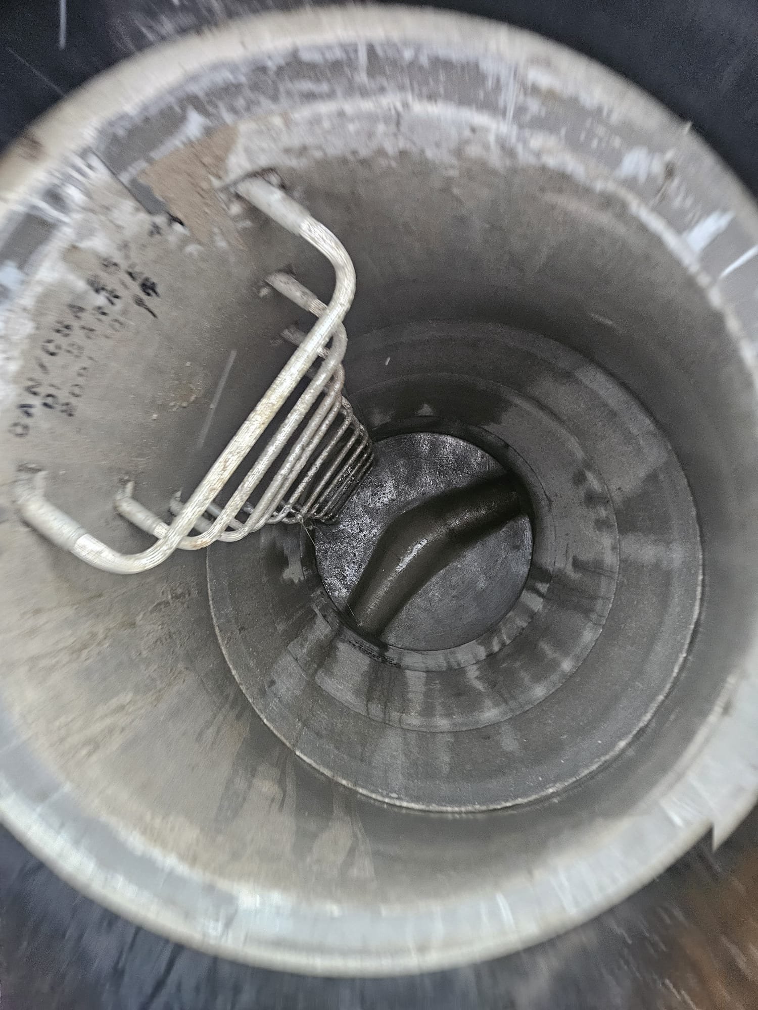 View inside a metallic industrial tank or pipe with a metal heating or cooling coil and a black pipe protruding at the bottom.